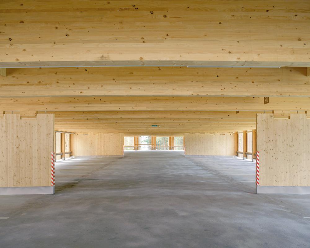 Über einem mit Betonpflaster belegten Parkplatz erhebt sich die zimmermannsmäßige Konstruktion. Träger und Stützen im Erdgeschoss sind aus Baubuche.