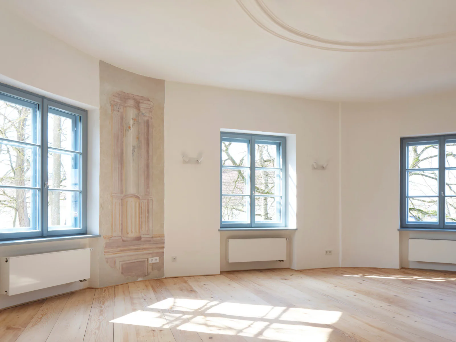 Der große Salon mit aufgearbeitetem Dielenboden. Umlaufende Architekturmalerei prägte den Raum.