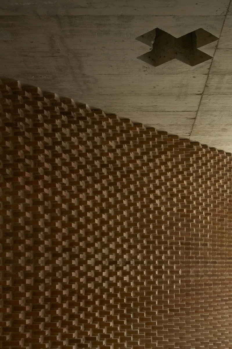 Eine schräge Wand mit Ziegelrelief weist den Weg zum Eingang.