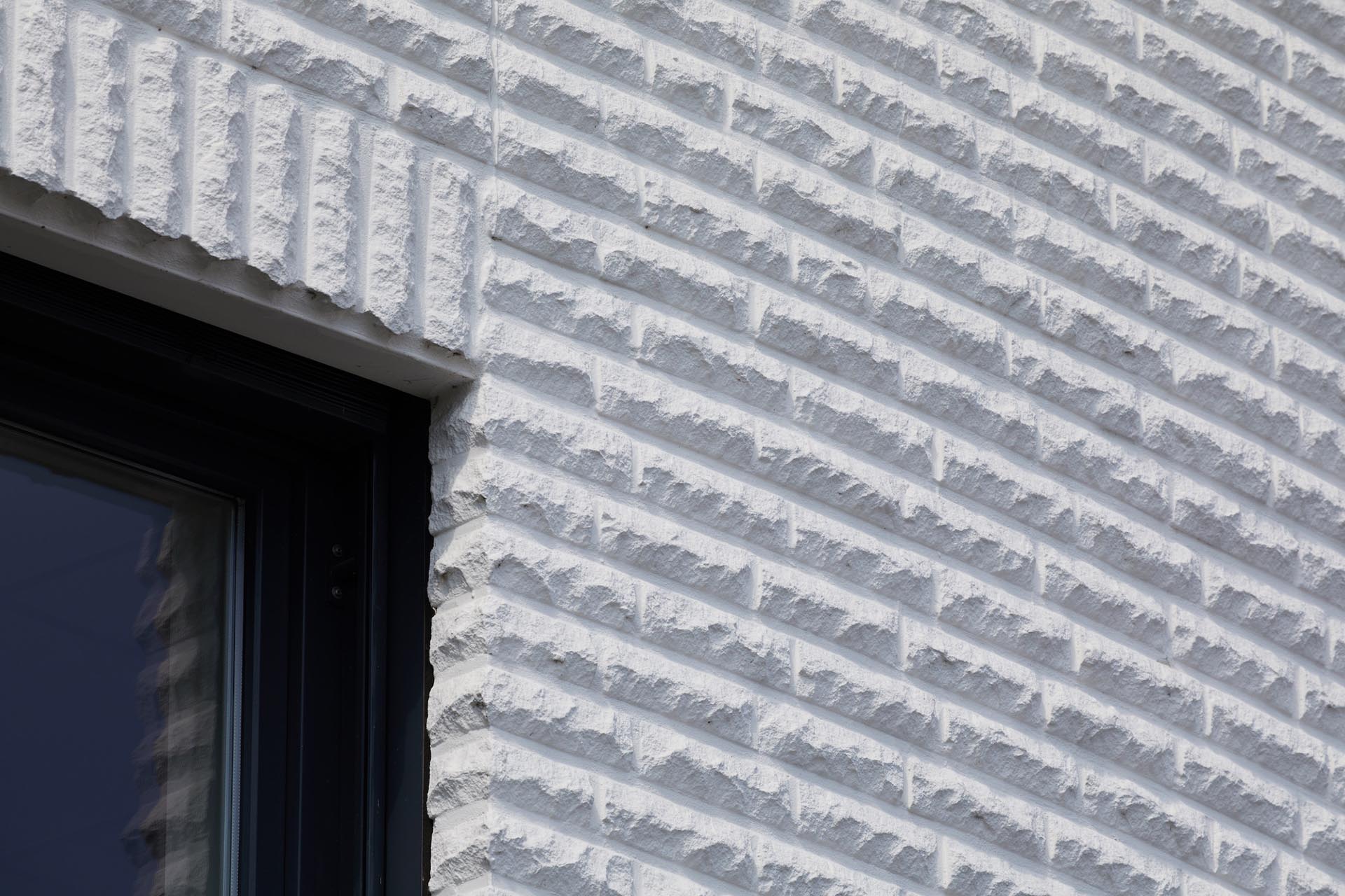 Weiße bossierte Kalksandstein-Verblender prägen die Fassade einer Wäscherei in Lohne nach Entwürfen von Staats & Petter. Die markante Oberfläche wirkt plastisch und kreiert ein Spiel aus Licht und Schatten.