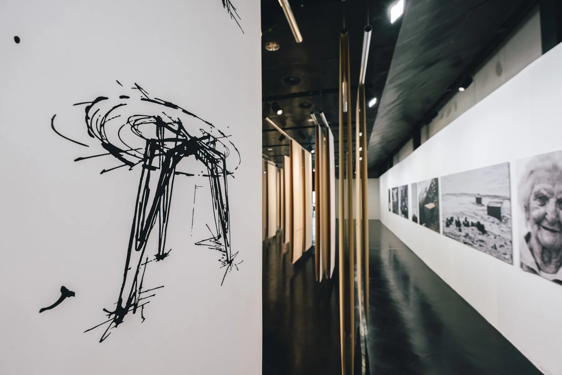 Die von der Decke hängenden Textilien zeigen Skizzen und Zeichnungen, an den Ausstellungswänden sind Fotos ausgestellt.