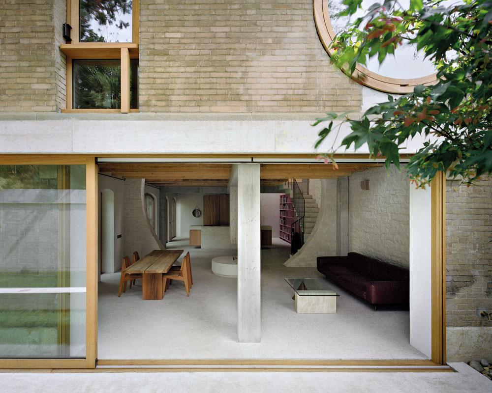 An der Stirnseite des Hauses öffnen große Glasschiebeelemente den Wohnraum zum Garten. Ihre Führungsschiene ist an einem Sichtbetonsturz vor der Fassadenebene befestigt.