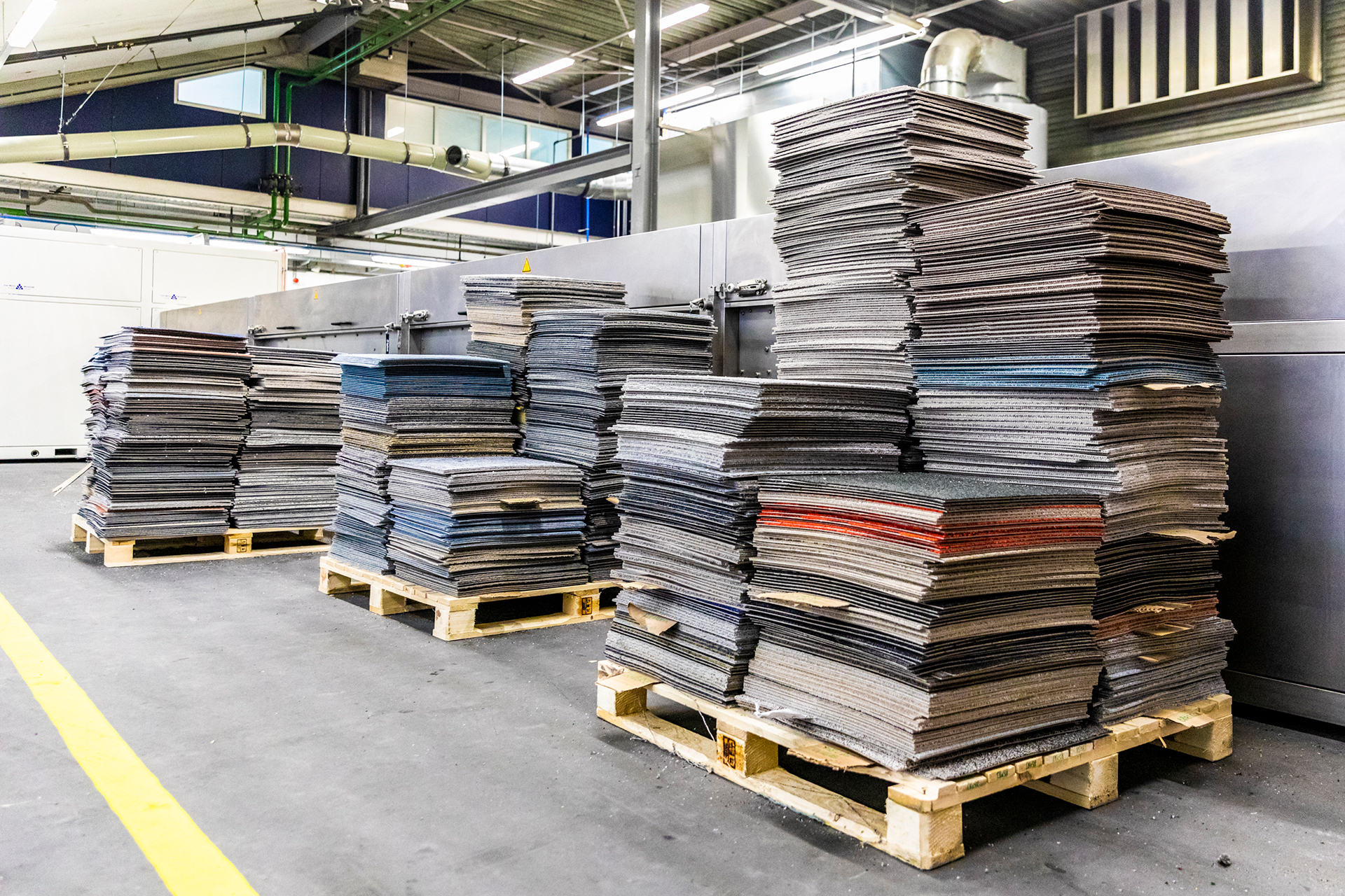 Gebrauchte DESSO Teppichfliesen von Tarkett werden einfach auf eine Palette gestapelt. Tatsächlich machen große Unternehmen vermehrt die Rücknahme und garantierte Wiederverwertung bereits heute zur Kaufbedingung für Neuware.