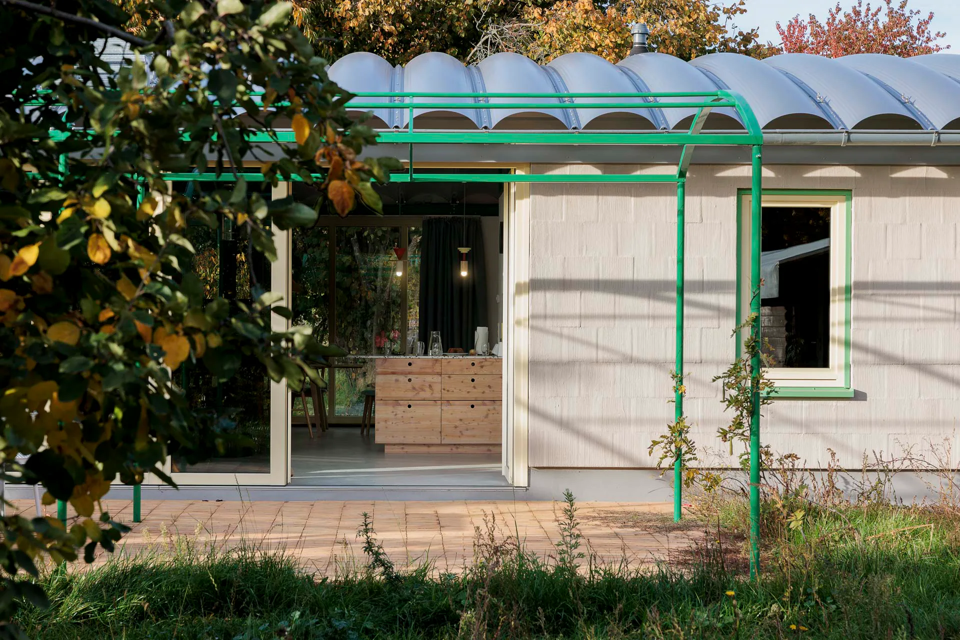 Die grüne Pergola greift die Tonnenform des Hausdachs auf. Die Außenwände aus Dämmziegeln wurden lediglich geschlämmt.