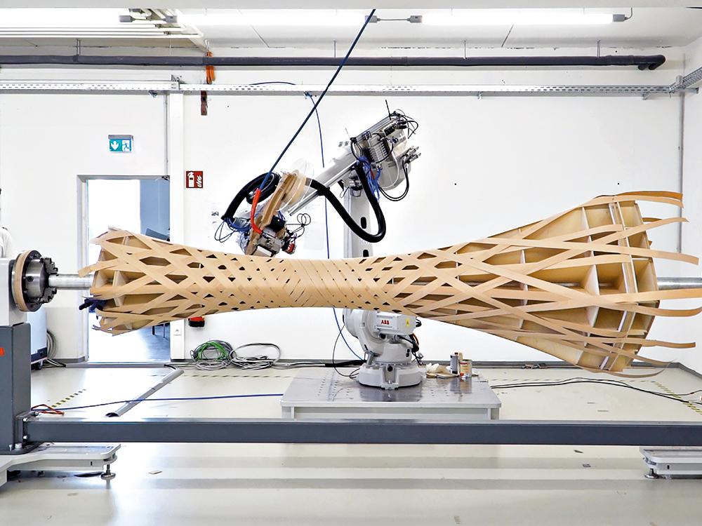 Bei dem Wickelprozess der Stützen aus Furnierholzbändern sind der 4 m lange Drehpositionierer und der Roboterarm so programmiert, dass sie synchron arbeiten.
