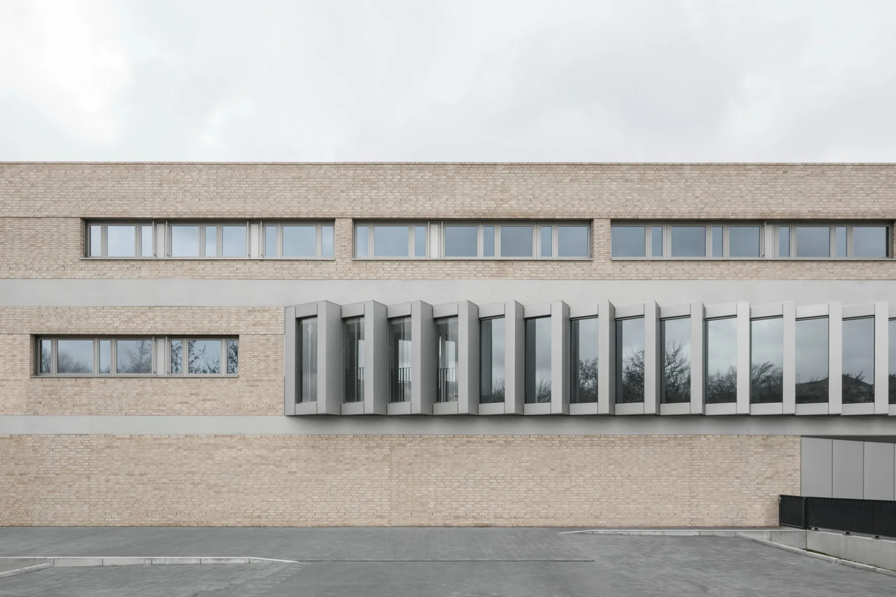 Bandfenster und Sichtbetonelemente gliedern die Klinkerfassade des Neubaus. Hinter dem ziehharmonikaartigen Fensterband befinden sich Schulungsräume.