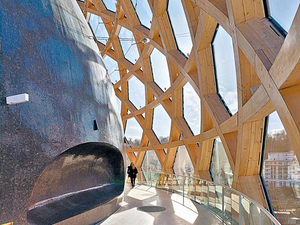 A spherical lattice structure consisting of timber and a sun sail on rails surround the auditorium of the cultural building La Seine Musicale, erected in 2017 near Paris.