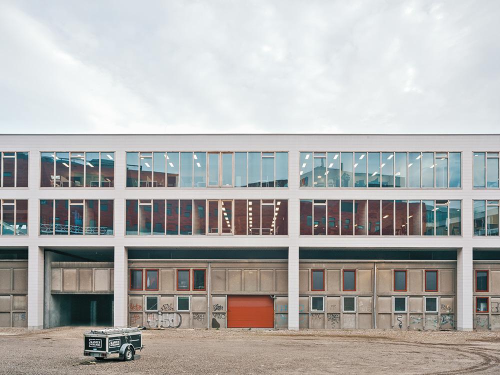 The two storey office facility design is structurally independent of the former warehouse: Seven truss beams are elevated by steel columns above the existing building.