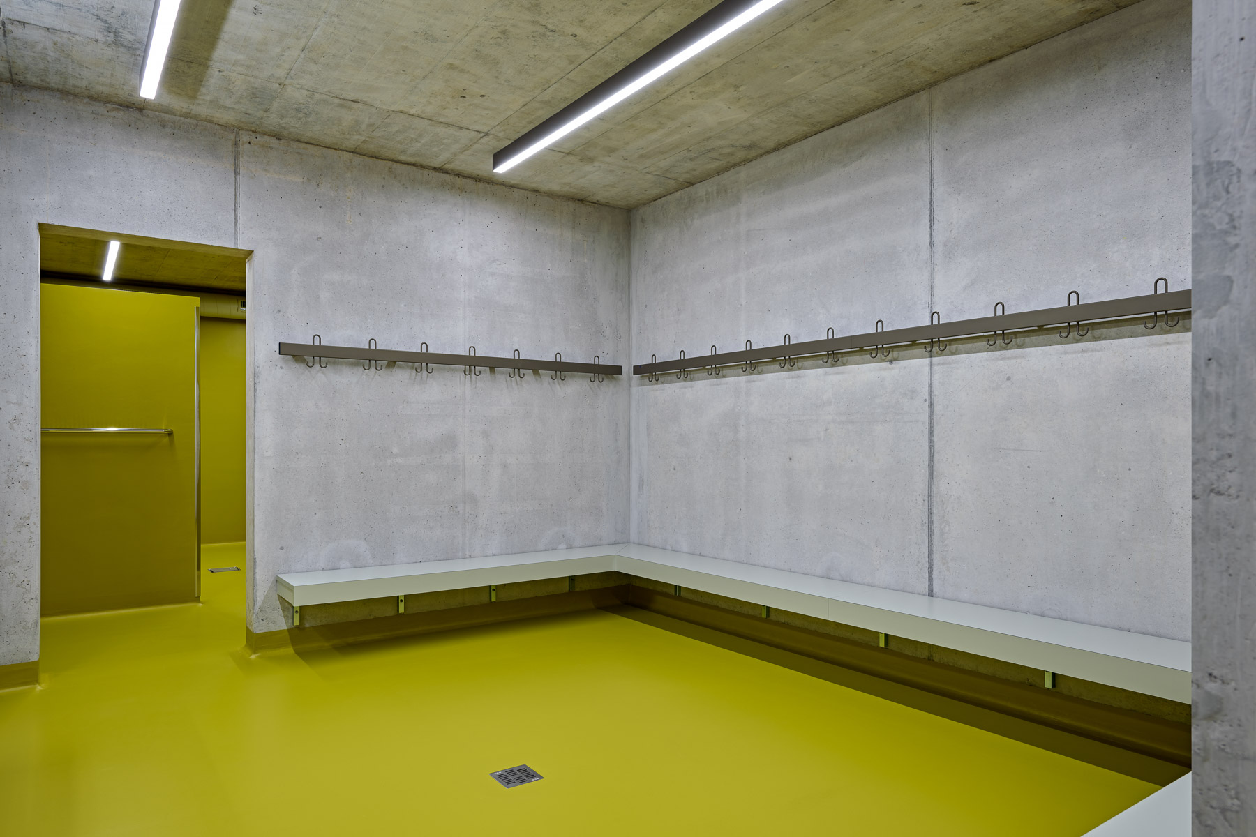 In den Umkleideräumen mit Nasszelle kontrastiert der rohe Beton mit knalligen Farben.