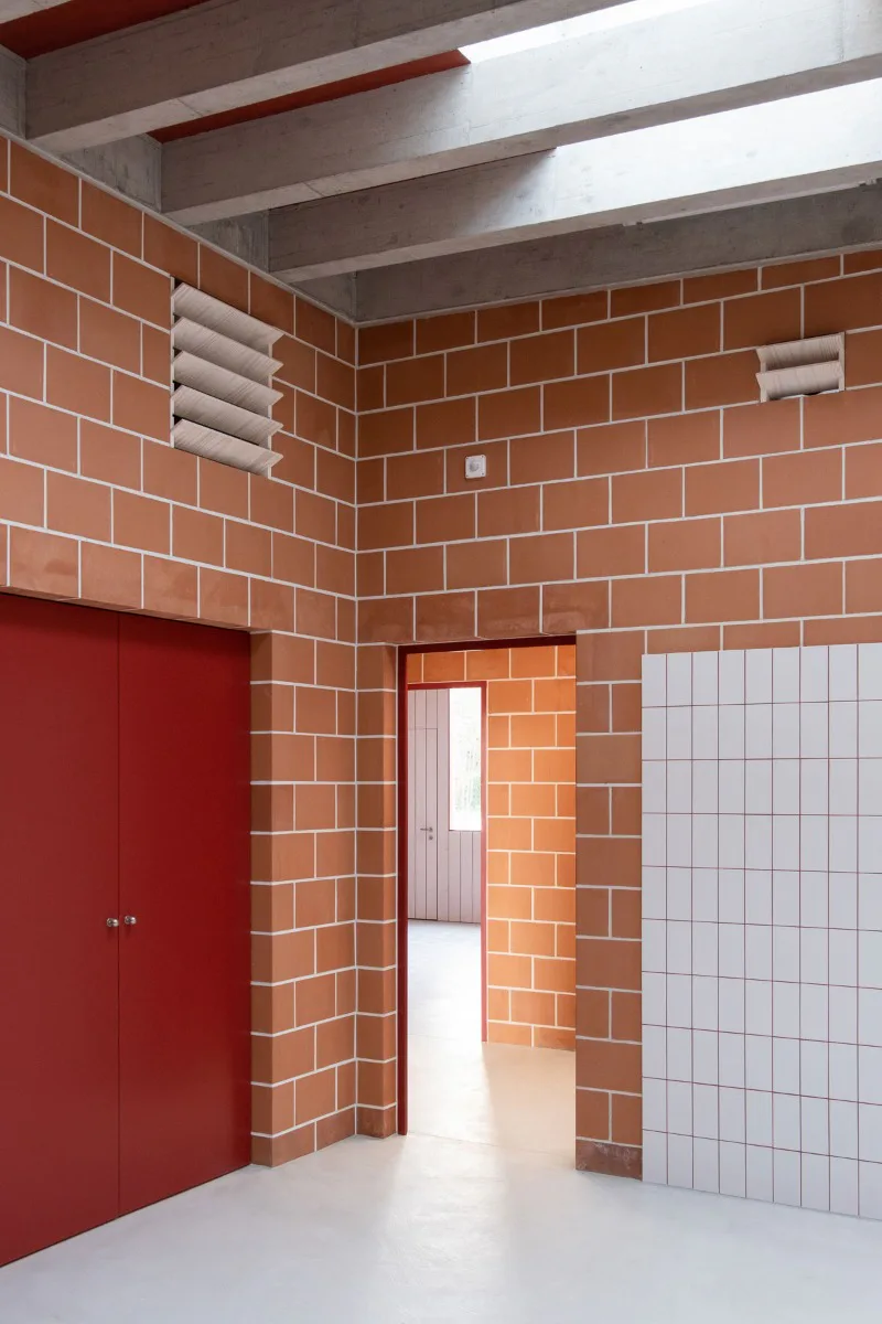 Rote Türen und Einbaumöbel sowie weiße Fliesen komplettieren die Materialpalette der Innenräume.