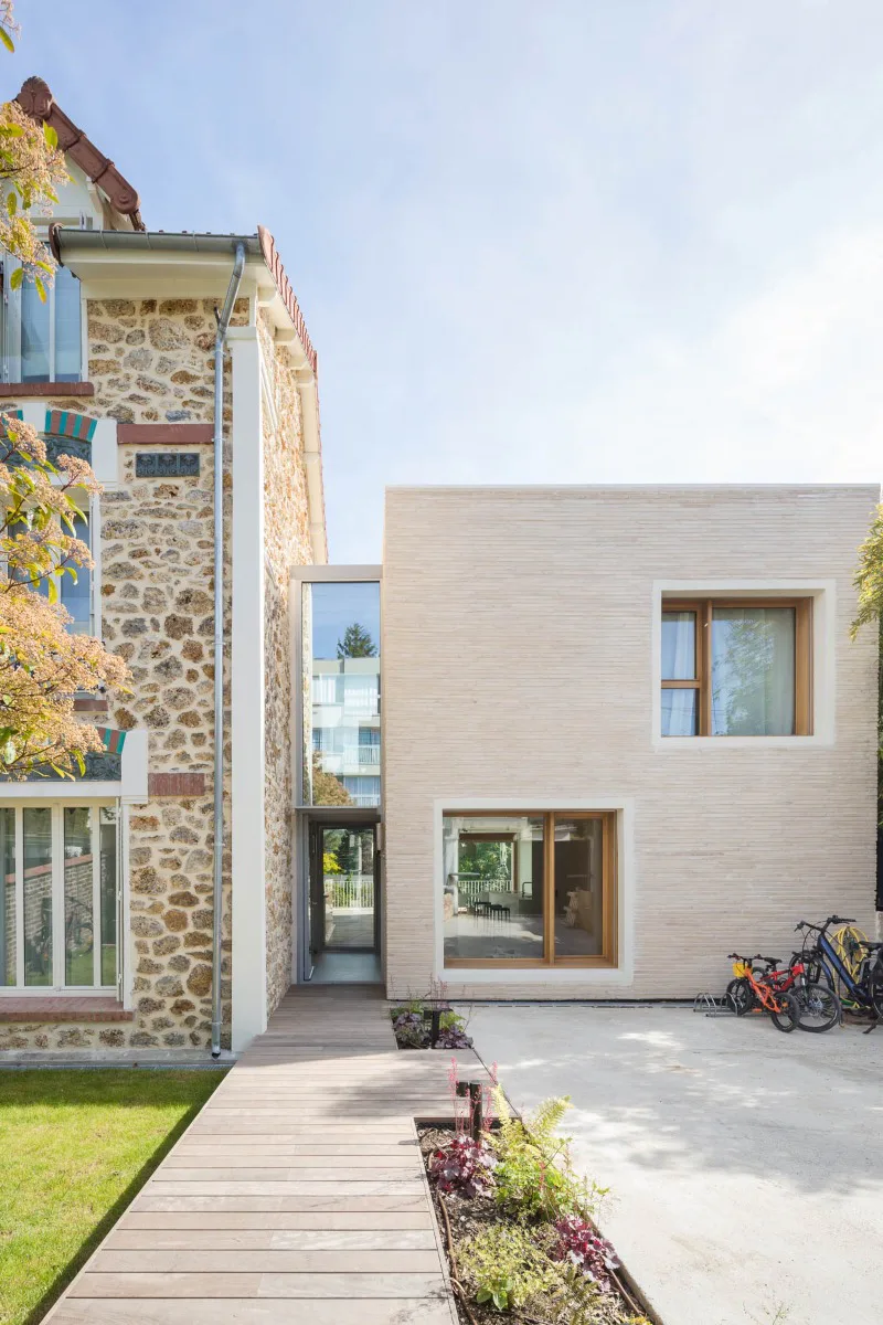 Bescheidener tritt das Haus an der Straße auf. Beigefarbenes Mauerwerk und weiße Fensterumrahmungen lassen Alt und Neu trotz aller Unterschiede als Einheit erscheinen.