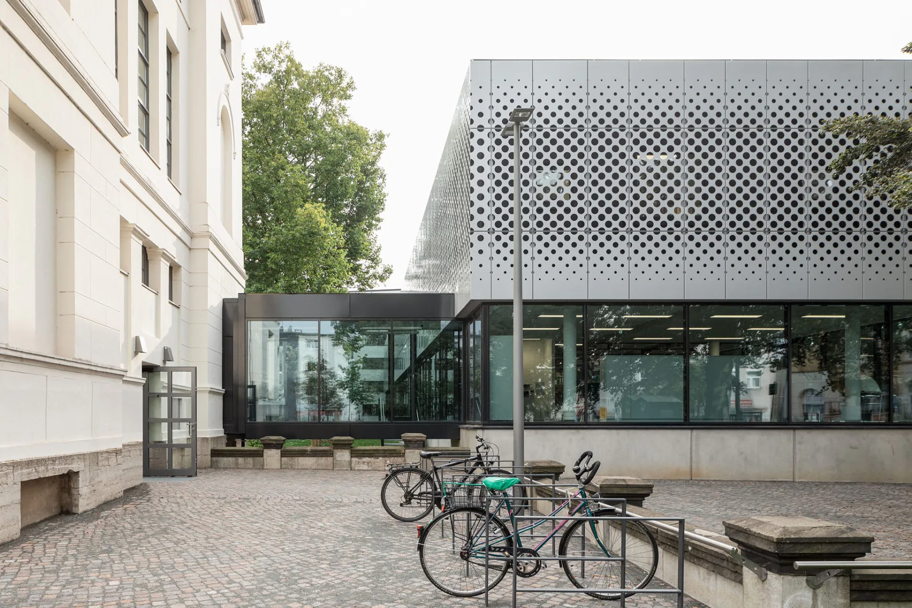 Ein Sockel aus Sichtbeton, ein Glasband und schließlich perforierte Metallbleche – so sieht die dreiteilige Schichtung der Bibliotheksfassaden aus.