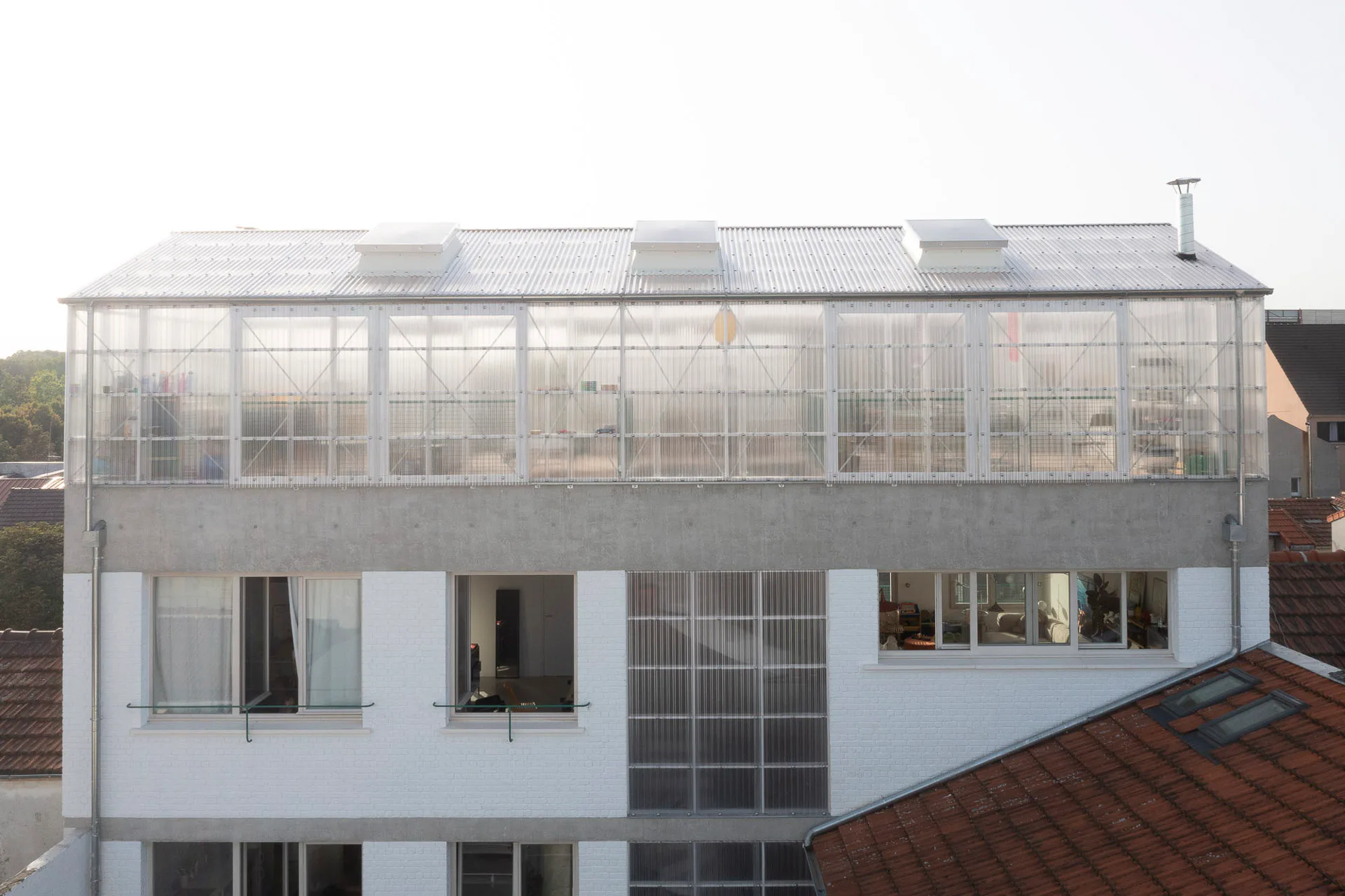 Die Polycarbonatplatten geben dem Dachaufbau ein Gefühl von Leichtigkeit, sodass Maison Commune trotz seiner Höhe weniger stark gegen die umgebenden Gebäude heraussticht.