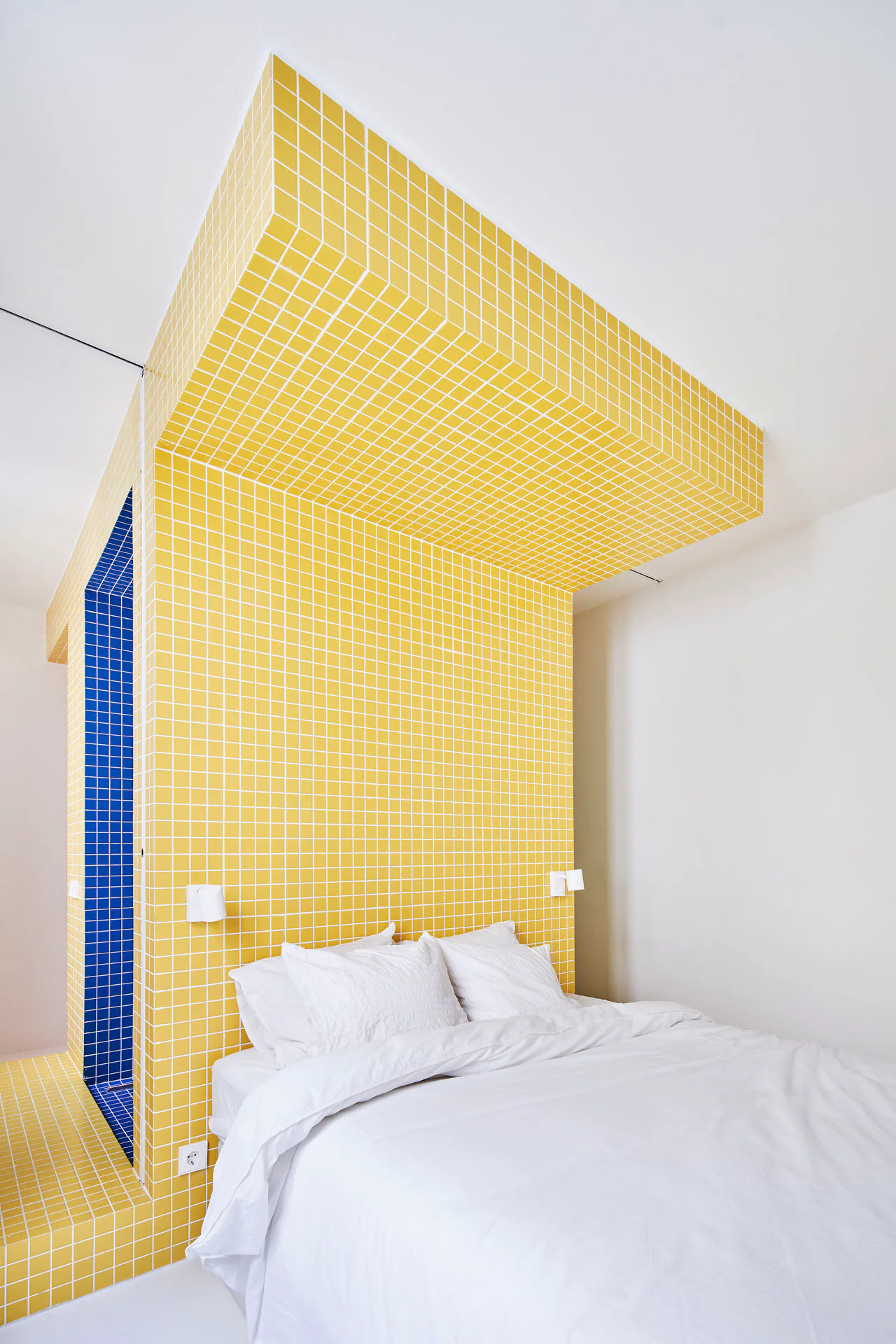Ein T-förmige Körper in einem der Schlafzimmer ist mit gelben Quadratfliesen verkleidet.