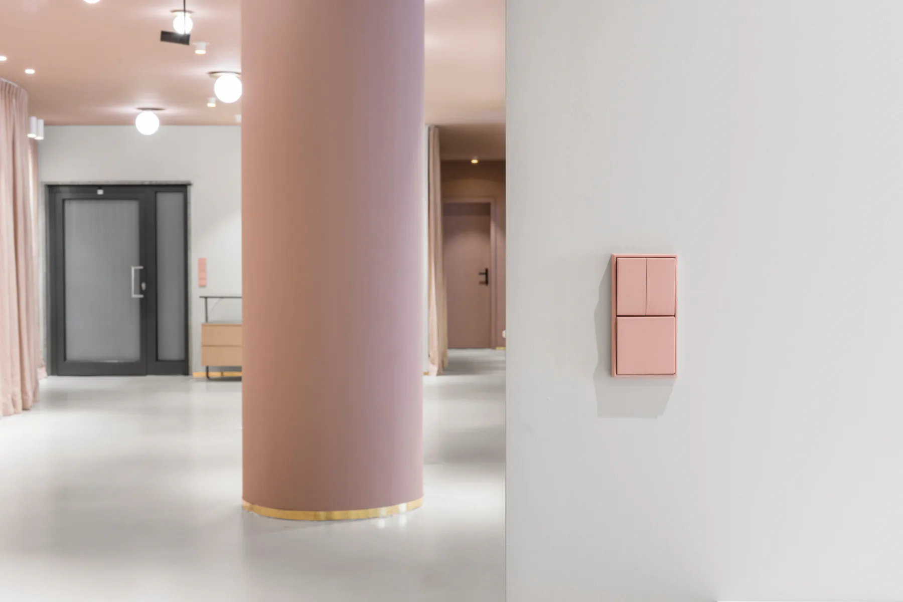 Stützen und Vorhänge in dunklem Rosé, dazwischen altrosa Lichtschalter auf weißen Wänden - das Farbkonzept der Emerson-Renaldi-Büroräume in Nürnberg.