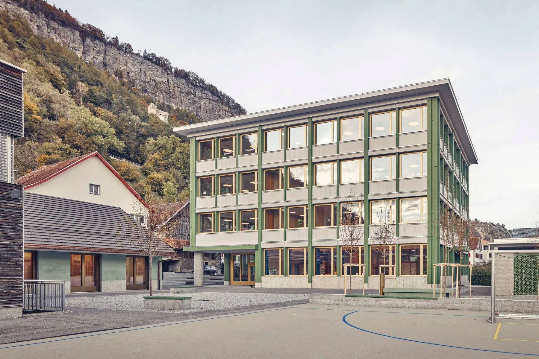 Das Schul- und Kindergartengebäude zeigt sich als Solitär mit großen Fensterflächen. Das kleinere Mensagebäude mit Satteldach öffnet sich zum Pausenhof.