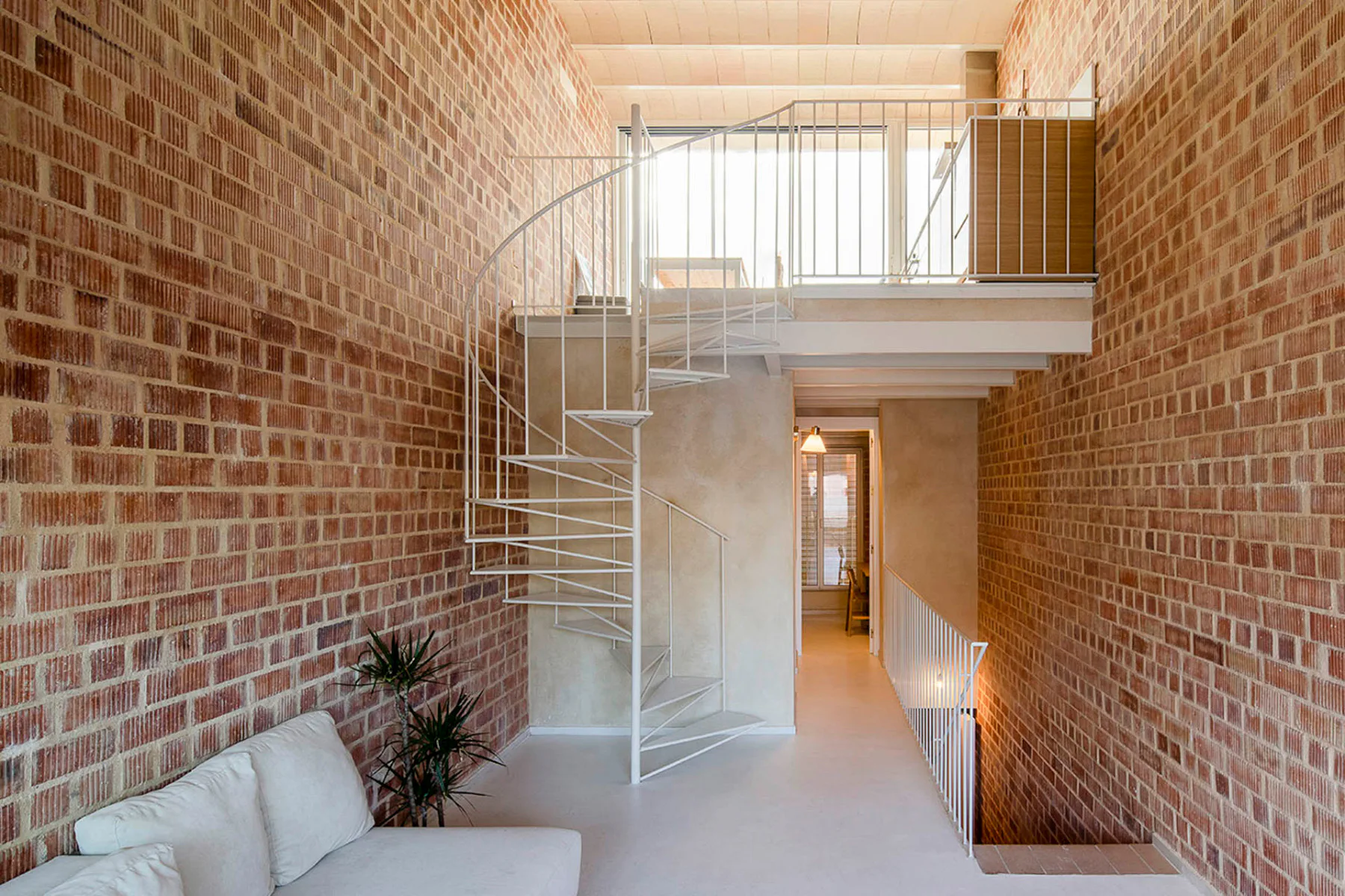 Vom Wohnraum führt eine Wendeltreppe aus Stahl hinauf zur offenen Küche unter dem gewölbten Dach.