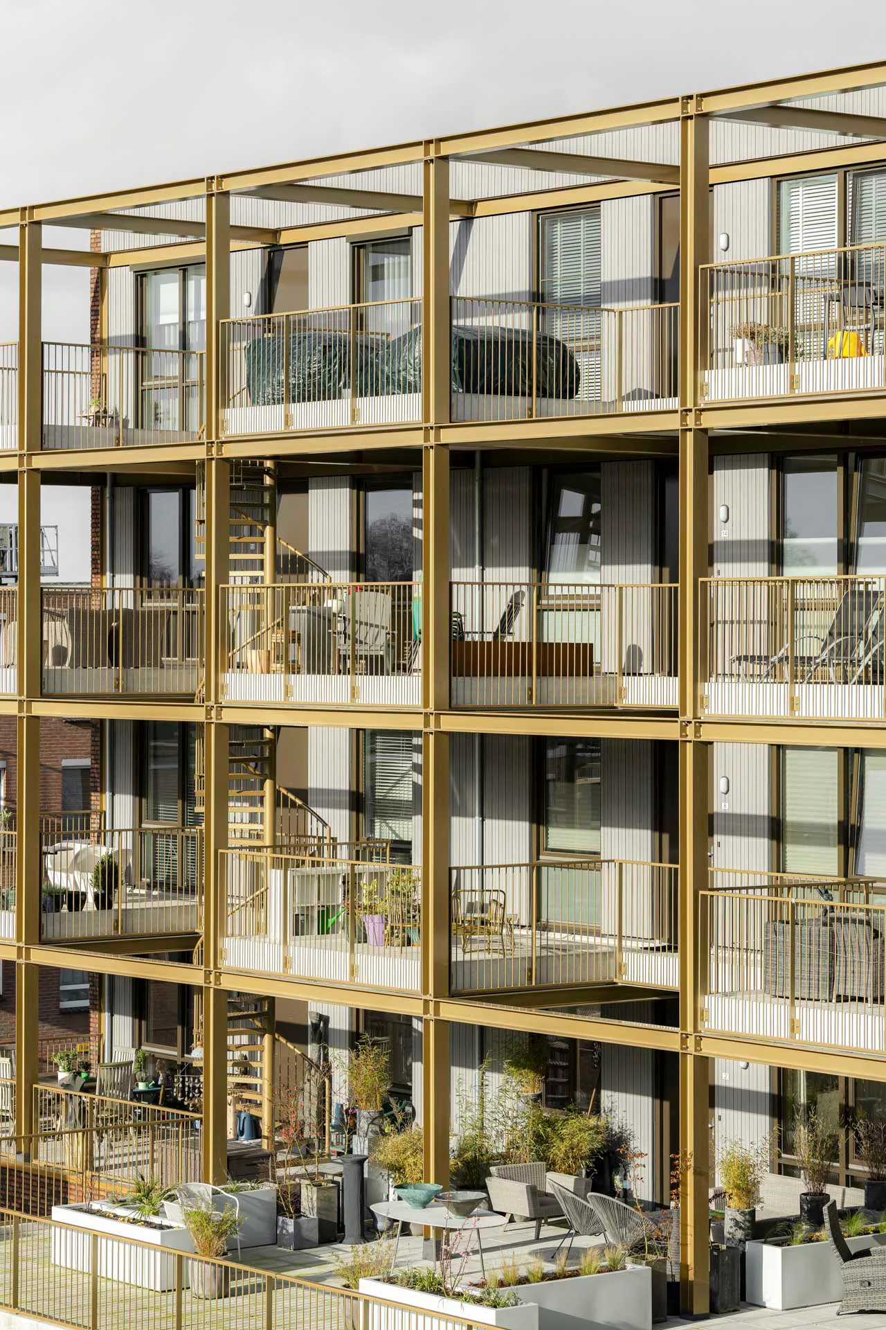 Die offene, goldfarbene Balkon-Stahlrahmenkonstruktion kontrastiert zum steinernen, schweren Charakter der übrigen Gebäudehülle.