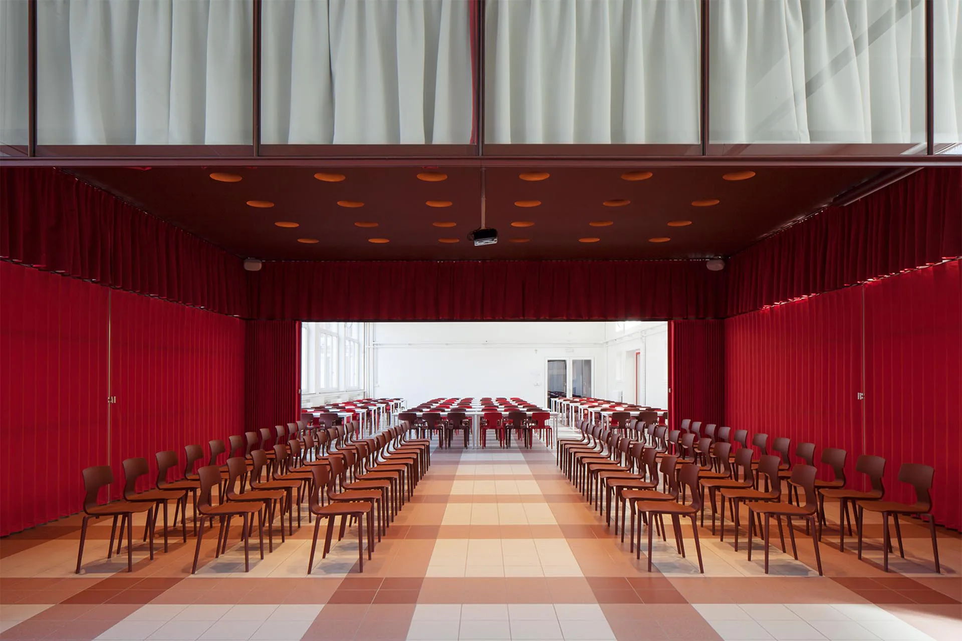 Die in den Raum eingestellte Box ermöglicht die Teilung des Saals in unterschiedlich große Räume. Die rote Farbe der Vorhänge im Inneren der Box erinnert an Theatervorhänge.