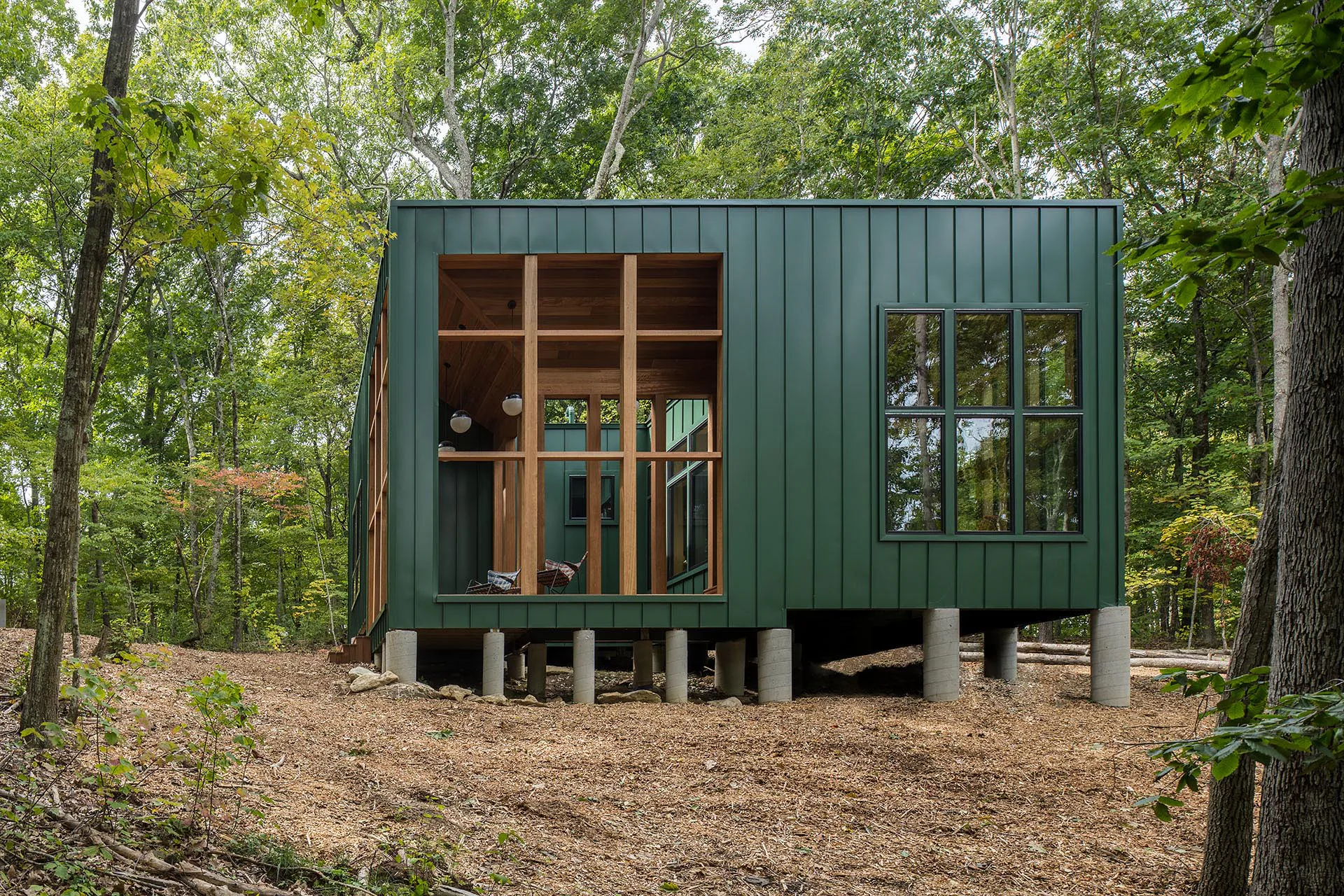 Einzelfundamente aus Beton heben den Holzkubus des Hauses über den Waldboden an.