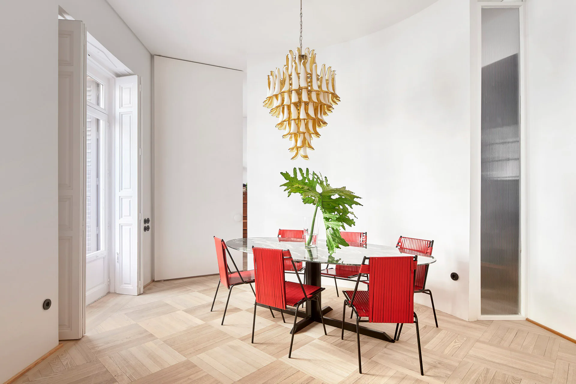Die roten Stühle am Esstisch bilden einen farbenfrohen Kontrast zu den monochromen Oberflächen auf Wand und Boden.