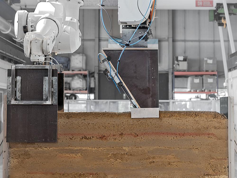 Im Digital Fabrication Laboratory (DBFL) der TU Braunschweig werden die Prozessschritte der Materialbeschickung, Verdichtung und Schalung in einem kooperativen robotischen Prozess erforscht.