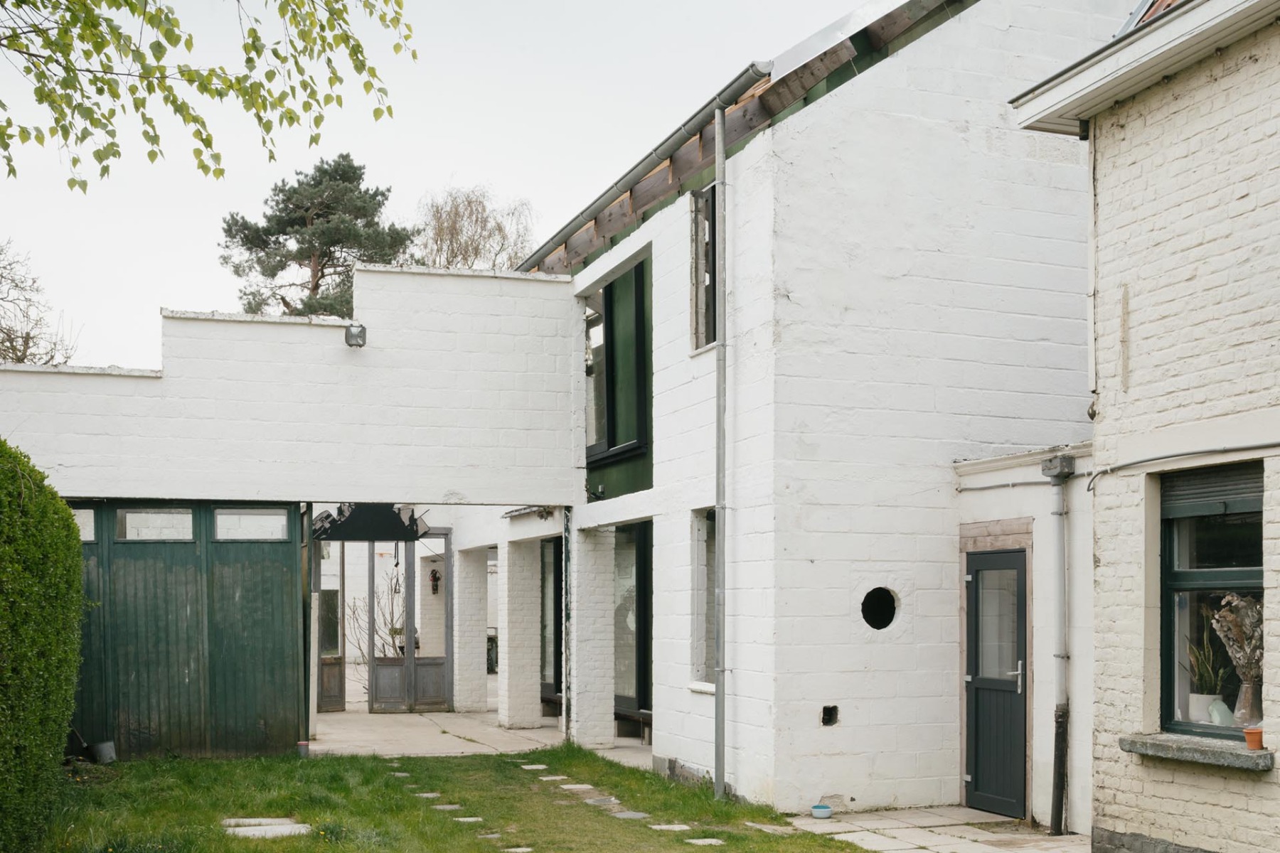 Holzhaus hinter alten Werkstattmauern in Flandern