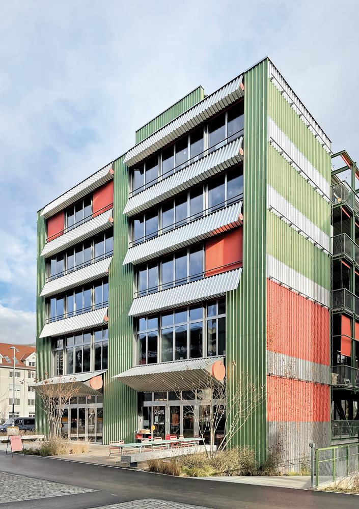 Die trapezblechverkleideten Kopfbauten erinnern entfernt an Containerstapel. In die dreieckig ausgestülpten Brüstungsverkleidungen sind Nistkästen integriert.