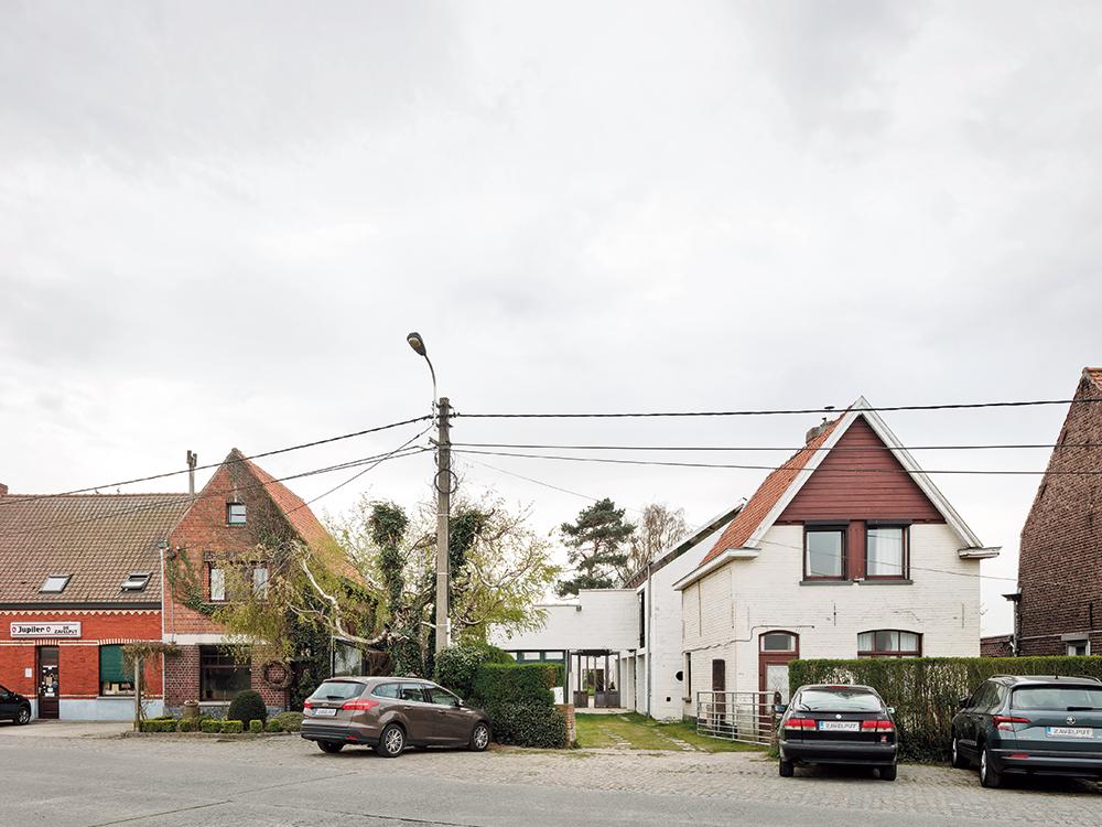 Das weiß gestrichene Sichtmauerwerk des Bestands liegt wie eine schützende, steinerne Schale um das Einfamilienhaus in Holzbauweise.