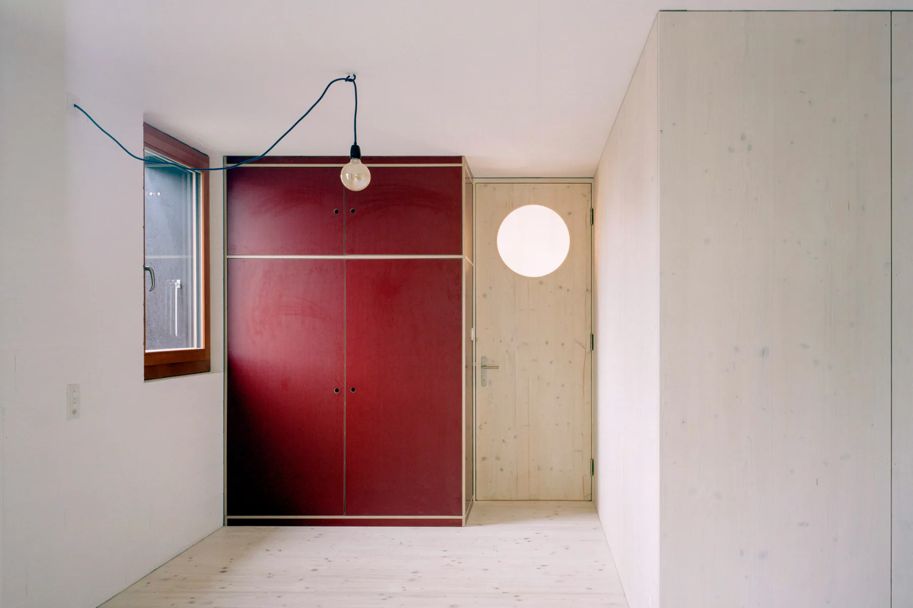 Ein roter Einbauschrank im Schlafzimmer kontrastiert mit den hellen Holzverkleidungen.
