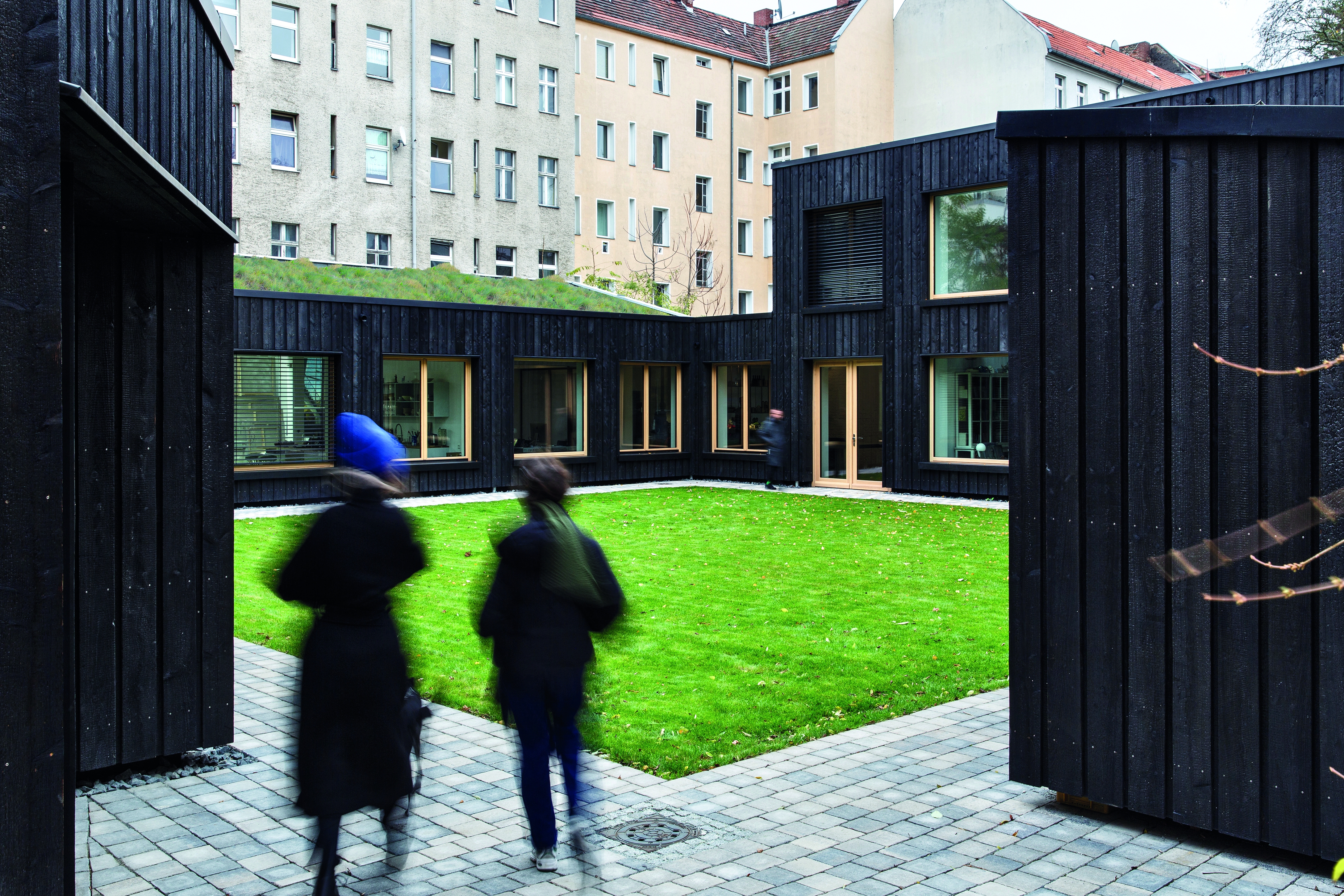 The backyard ensem- ble was first used as garages, then as metal workshop and now as a combined dwelling, office and studio build- ing. During the conver- sion it received a uni- form charred timber facade.
