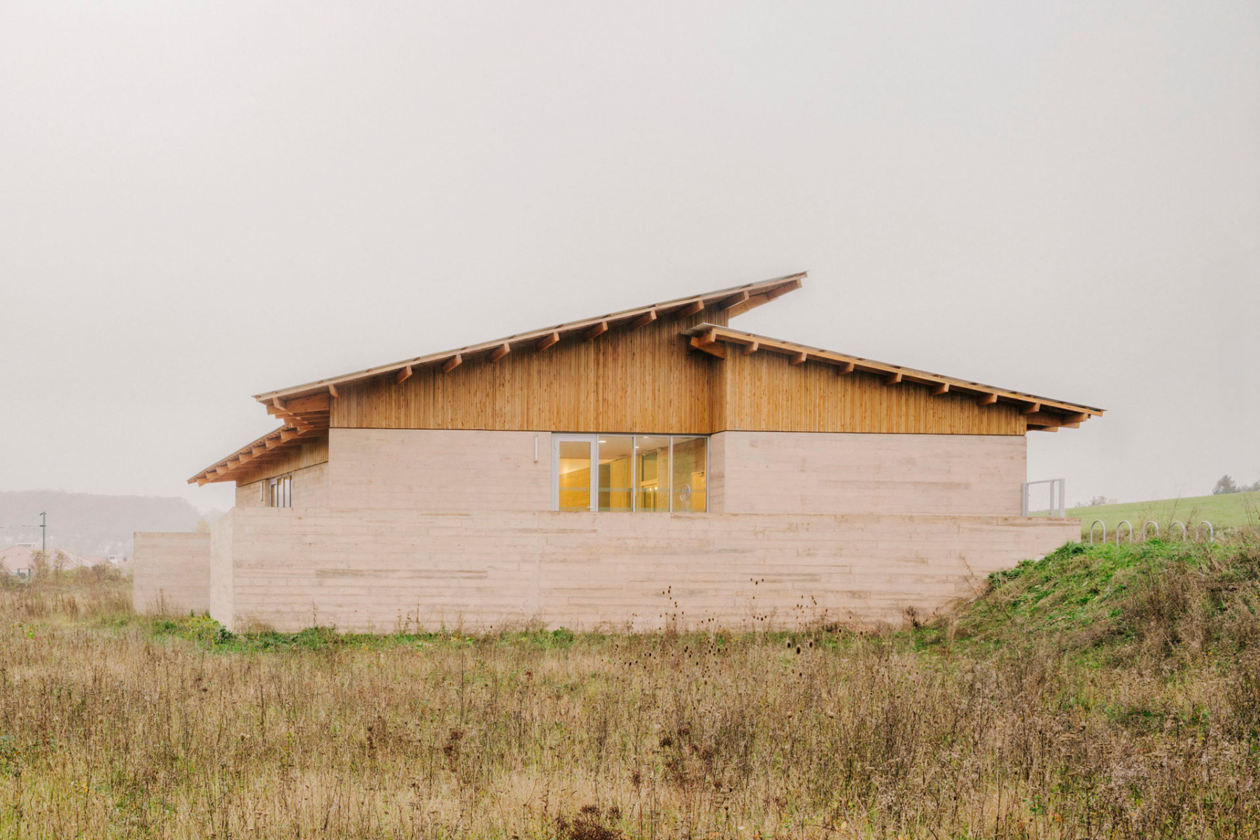 Zwei gegeneinander verschobene Pultdachflächen überspannen den Neubau, der zwischen den Ortsteilen auf dem freien Feld liegt.
