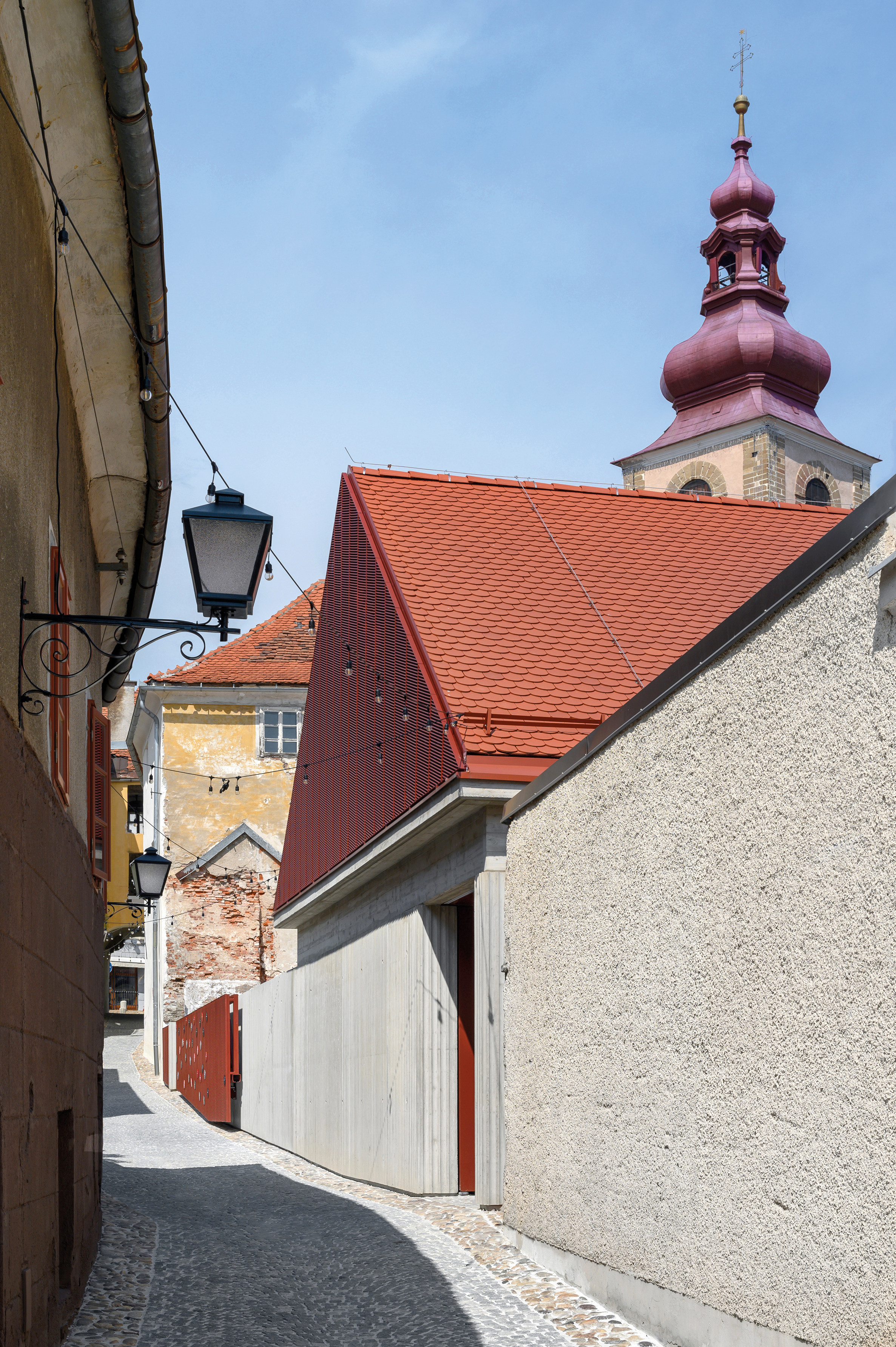Die wellenförmig profilierte Sichtbetonfassade des großen Veranstaltungssaals harmoniert mit den rauen Putzoberflächen des Nachbargebäudes.