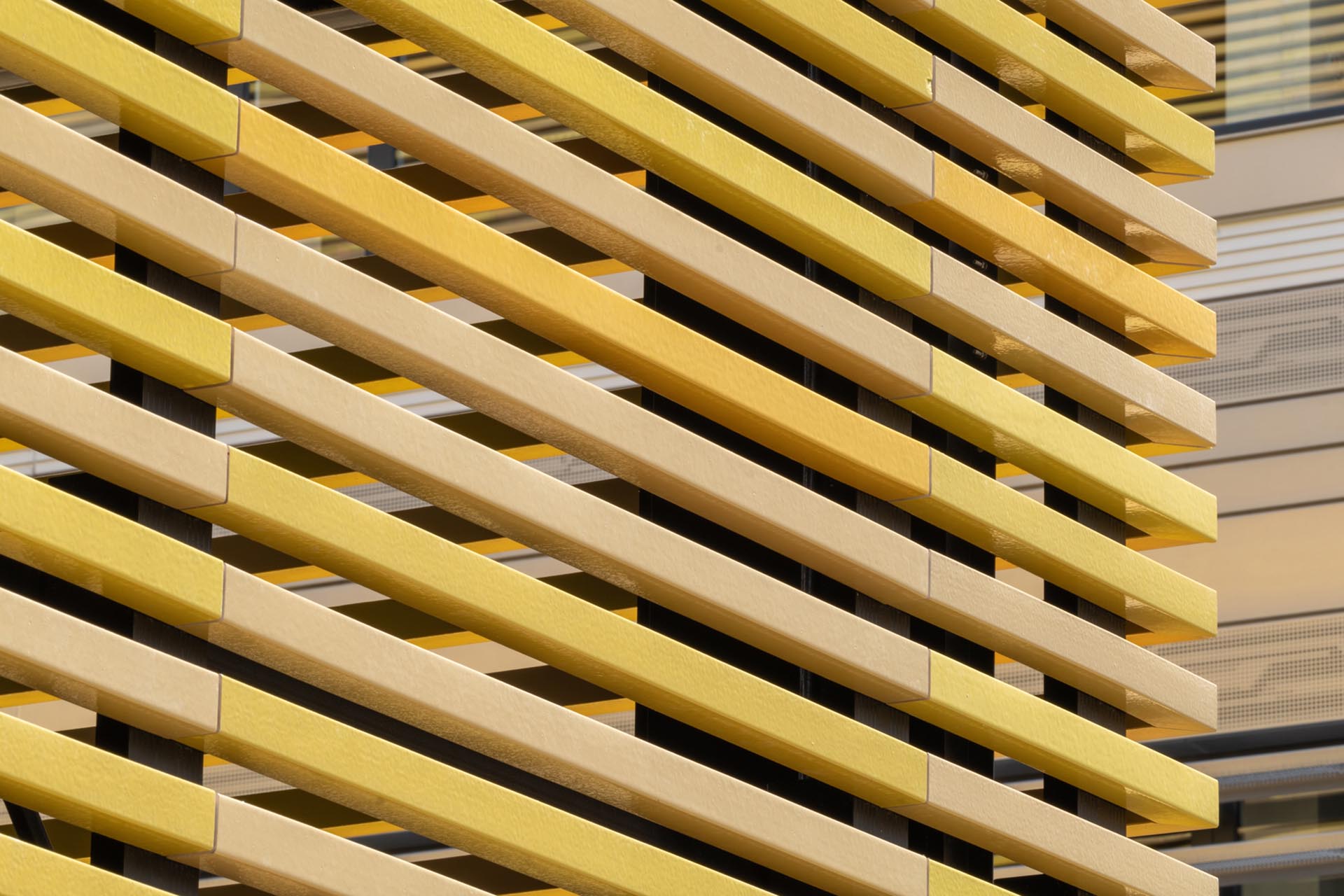 Fassadenbekleidung aus quadratischen, hohlen Keramikstäben, sogenannten Baguettes, in fünf Gelbtönen (RAL 1002, 1004, 1012, 1018 und 1021).