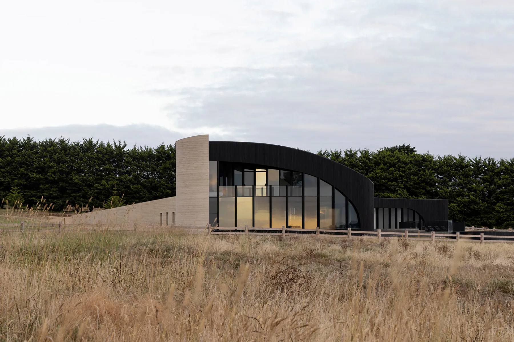 Eine lange Mauer aus Stampflehm sowie eine Fassade aus verkohltem Holz umhüllen das Peninsula House.