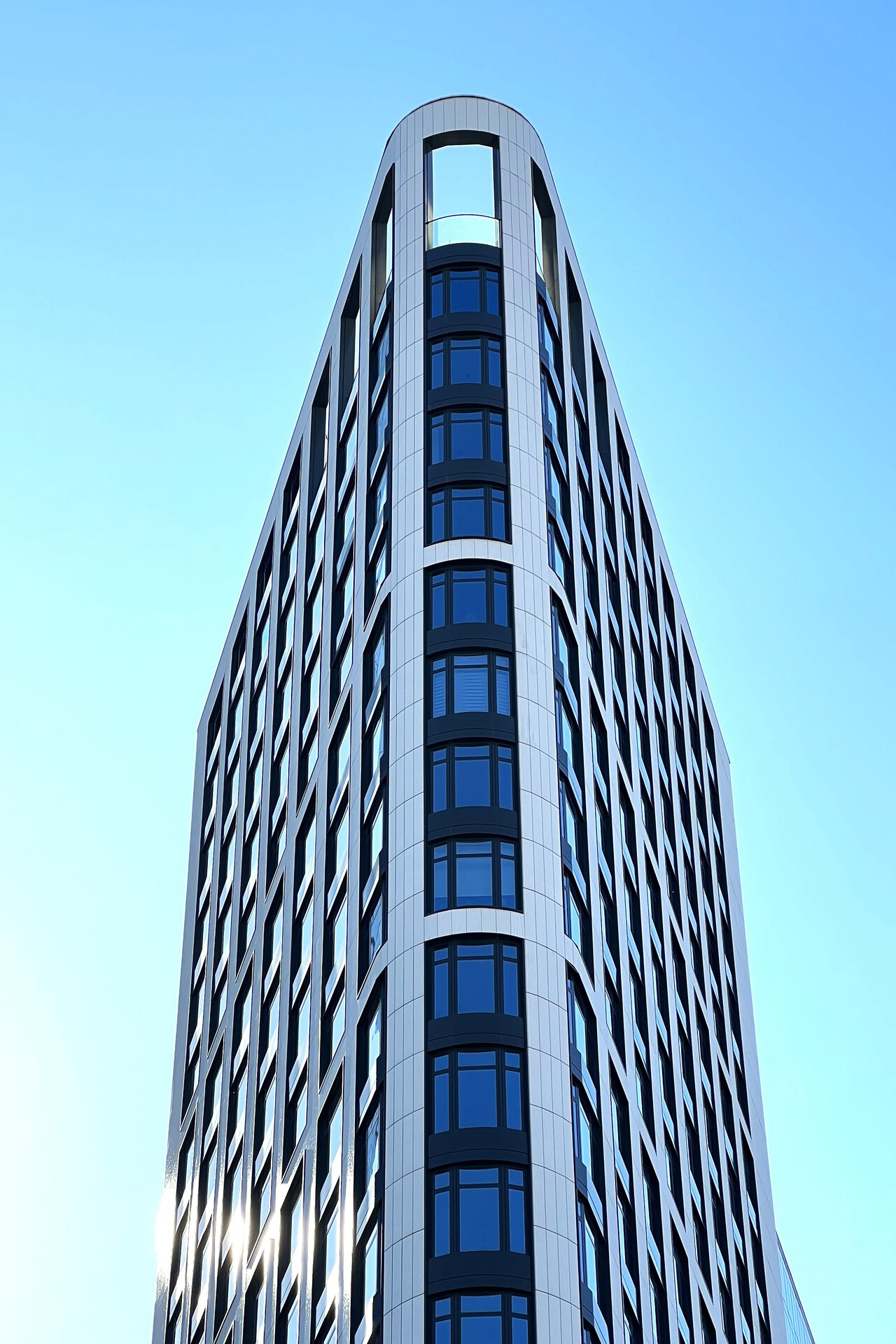Das Hochhaus steht auf einem engen Eckgrundstück. Mit der abgerundeten Außenecke zeichnet es dessen Form nach.