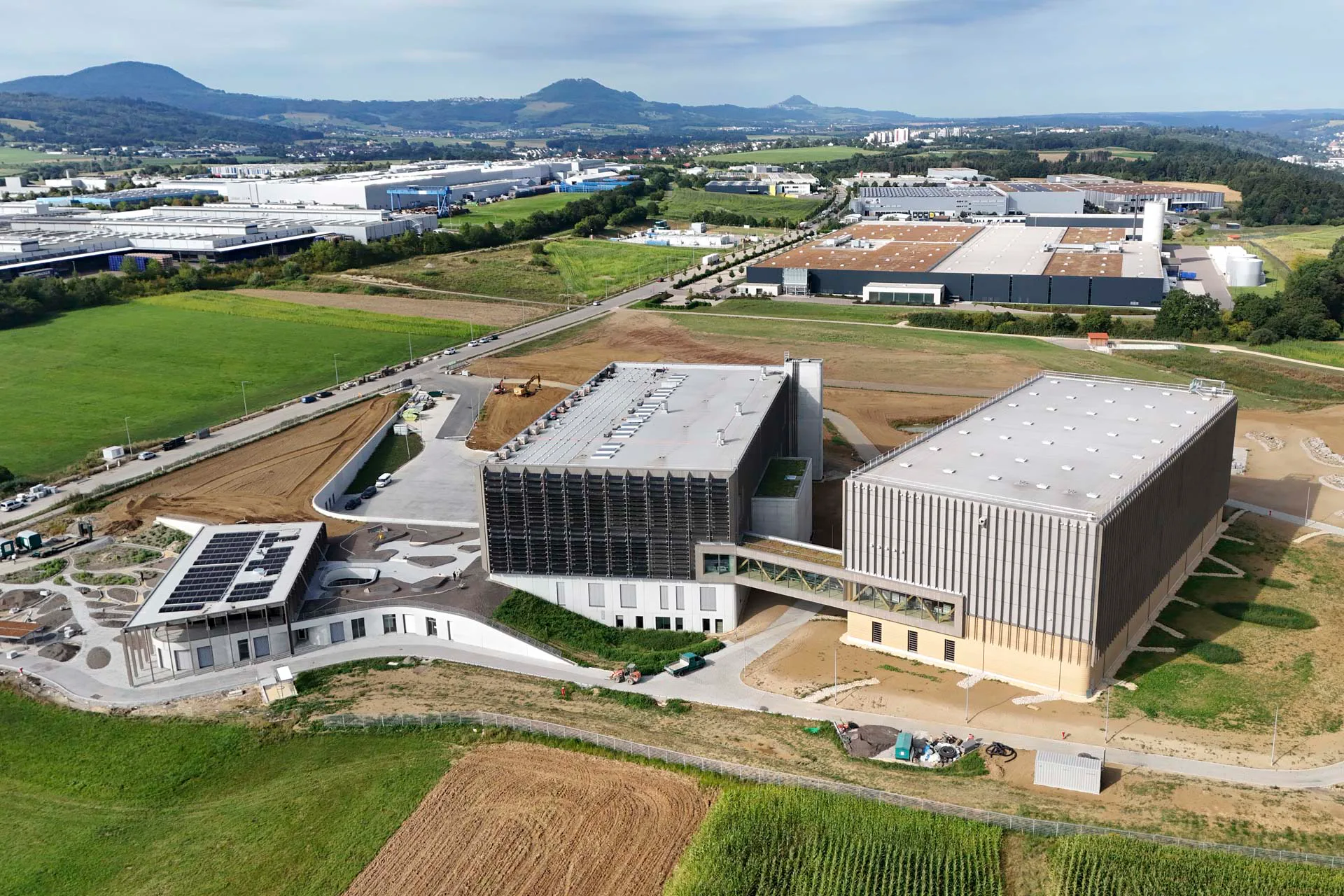 Das Logistikzentrum besteht aus drei Baukörpern: Das kürzlich fertiggestellte Hochregallager (rechts) ist über eine Brücke mit dem Produktionsgebäude (Mitte) und dem Verwaltungsgebäude (links) verbunden.