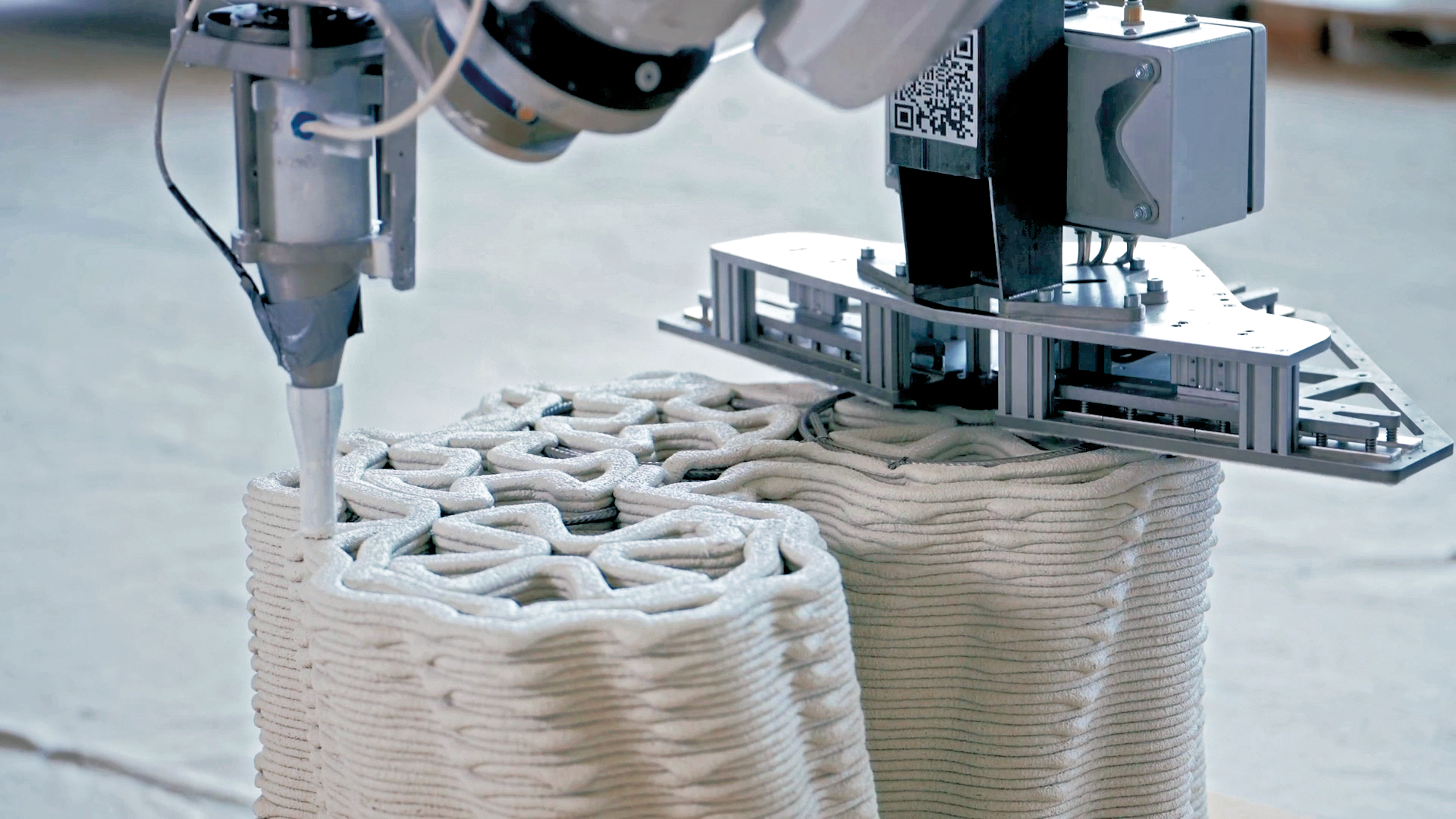 Der Beton wird während des 3D-Drucks armiert. Während der Roboter links den Beton aufträgt, platziert der andere die horizontale Bewehrung zwischen den Betonschichten.