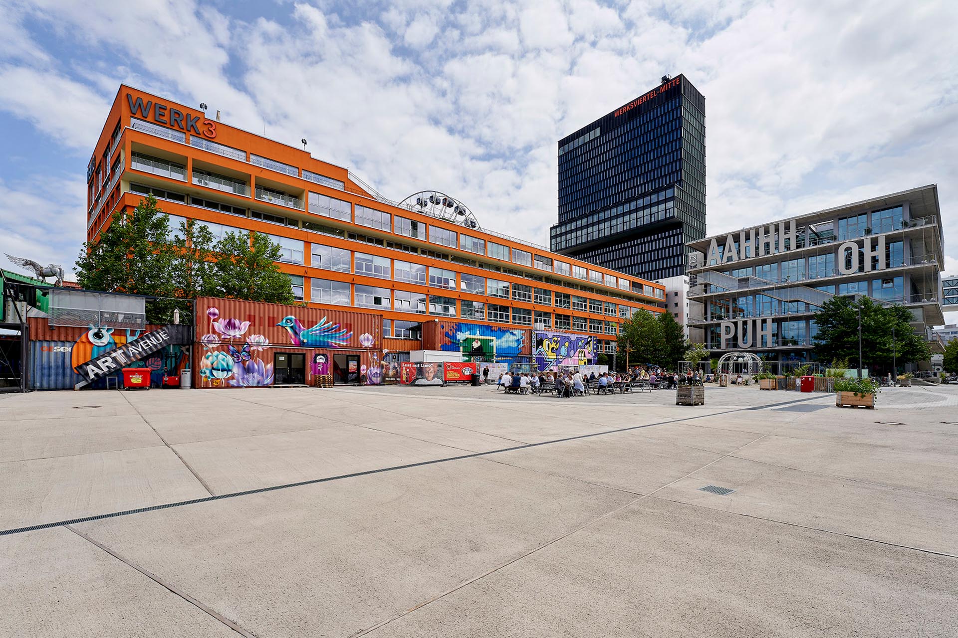 Außenansicht des WERK3 mit Büros und vielseitiger Gastronomie, Werk 4 mit einem Hostel und einem Hotel, Werk 12 mit Büros und Fitnessclub (inkl. Schwimmbad) sowie des Container Collectives im Vordergrund mit Ateliers und Gastronomie.
