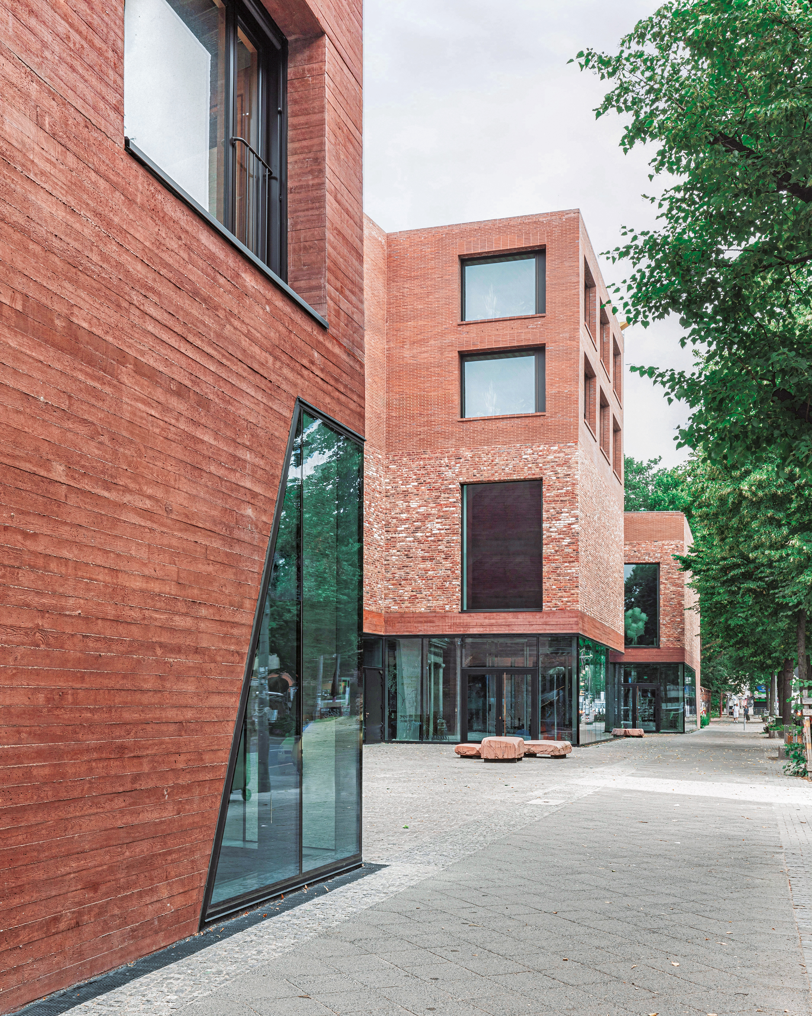 Zweierlei Ziegel und roter Sichtbeton bilden bei der Spore Initiative (hinten) eine dreiteilige Fassadengliederung. Sie spiegelt den inneren Aufbau des Gebäudes mit Café, Ausstellungsräumen sowie Bibliothek und Verwaltung wider.