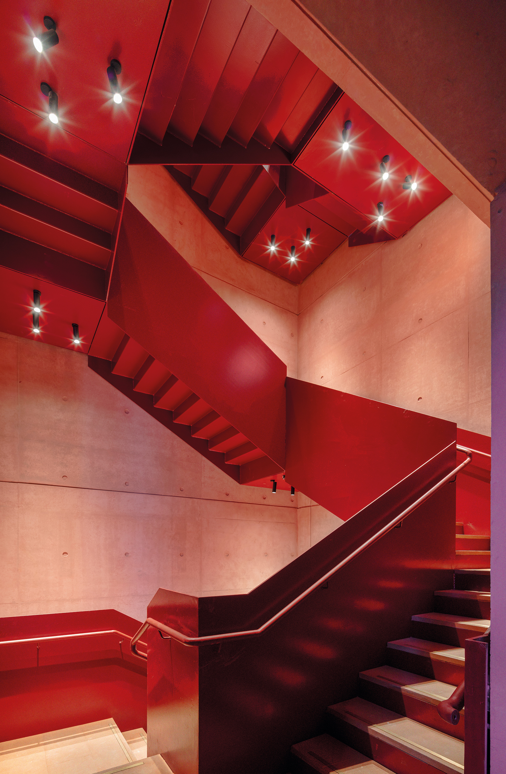 Die skulpturale Treppe aus leuchtend rotem Stahlblech setzt einen auffälligen Akzent in der mineralischen Hülle.