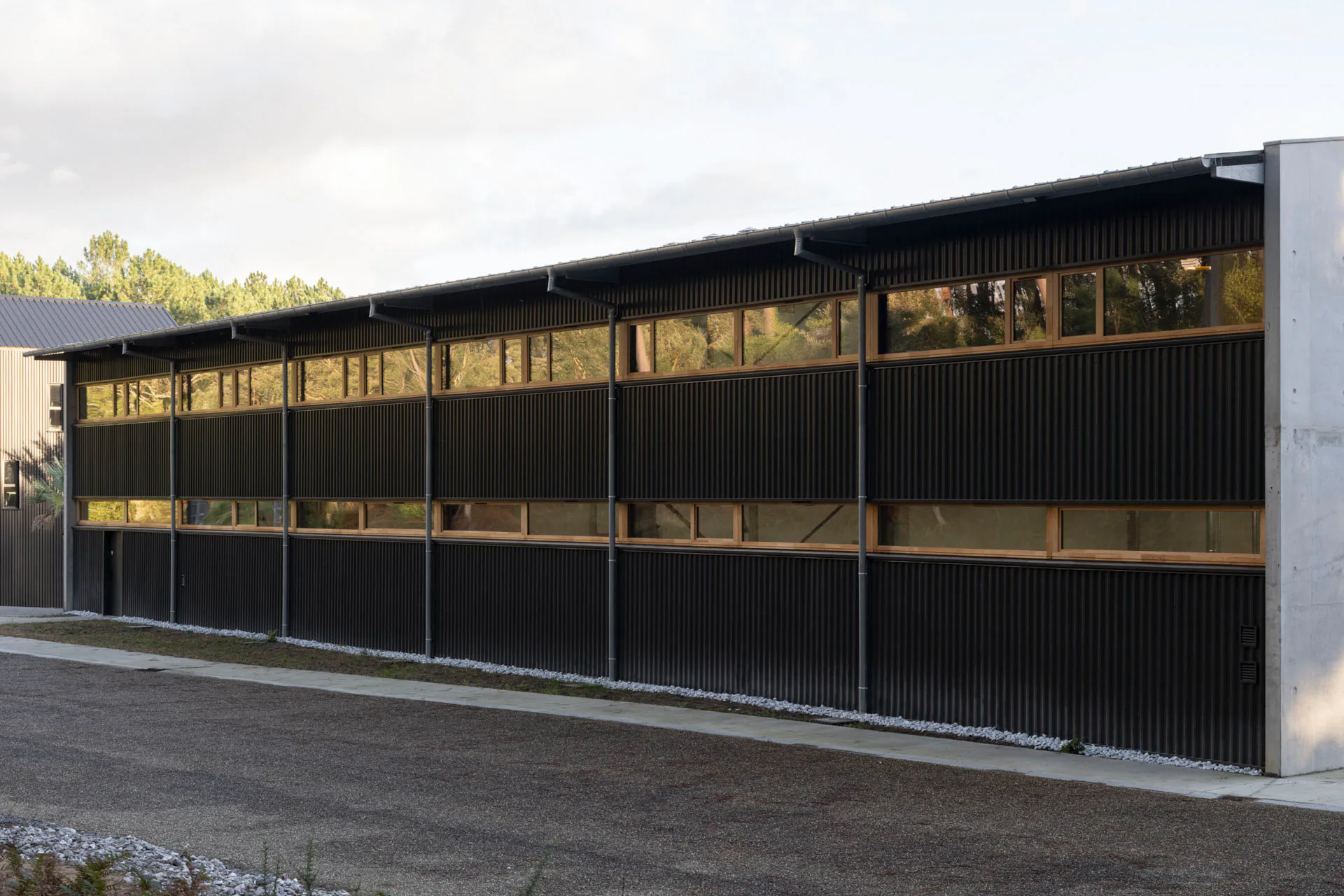 Dunkle Metallverkleidungen, horizontale Fensterbänder und das regelmäßige Raster der Regenfallrohre gliedern die Längsfassaden.