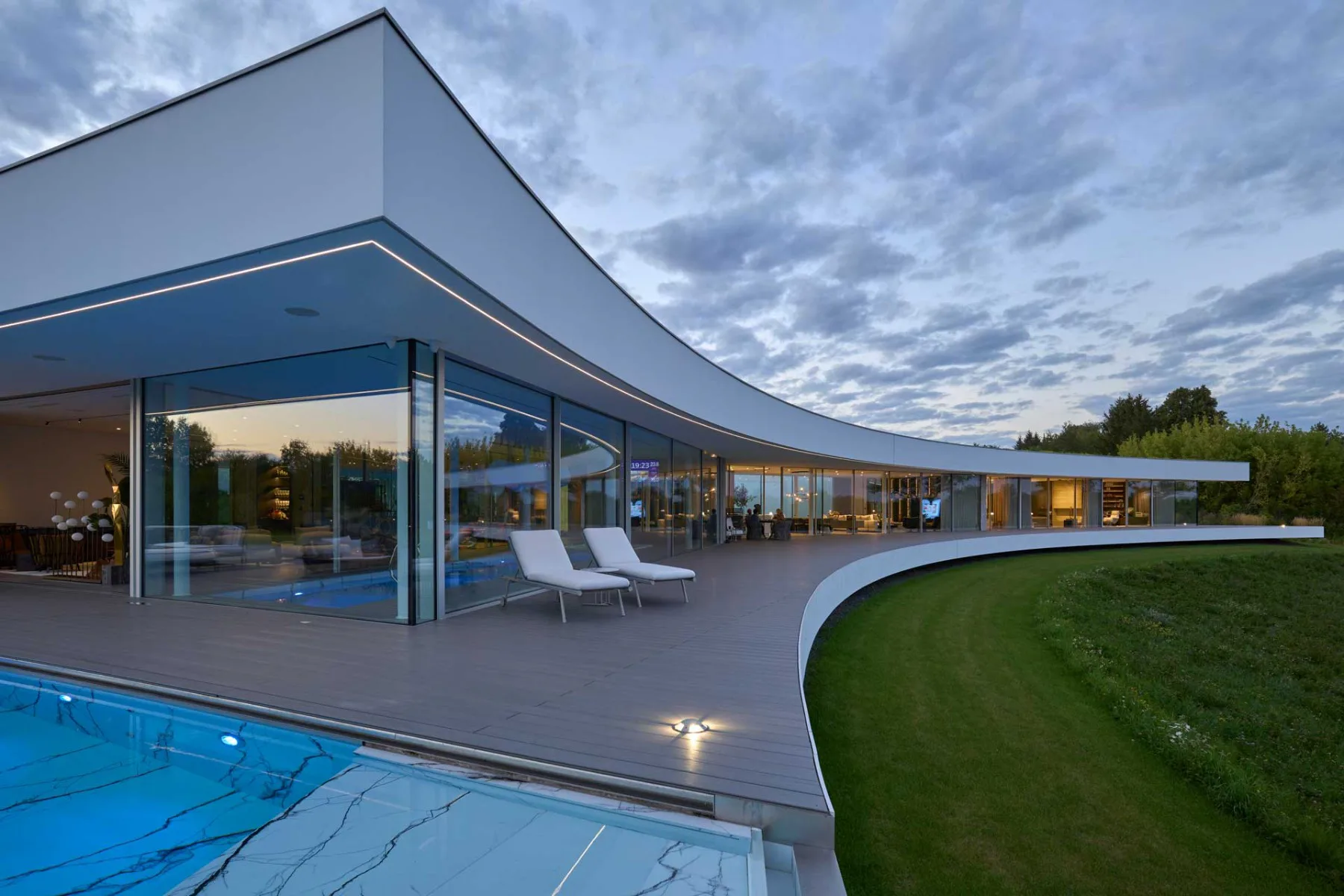 Die geschwungene Form, die der Biegung des Flusses folgt, verfügt über eine vollständig überdachte Terrasse, die sich über mehrere hundert Meter erstreckt und das Haus zur weiten Landschaft hin öffnet.