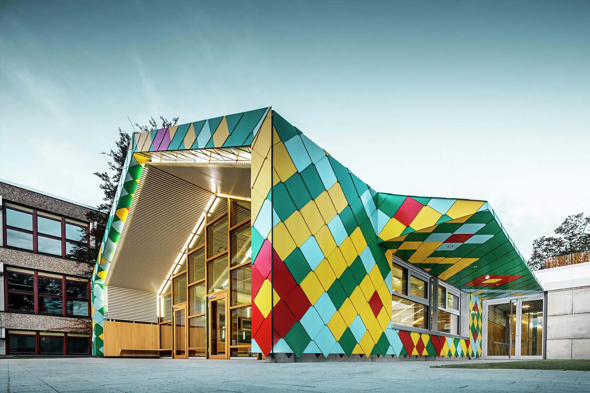 Schulmensa in Stuttgart mit bunter Außenhülle aus Dach- und Wandrauten 44 x 44 in den Sonderfarben Ginstergelb, Karminrot, Normminzgrün und Pastelltürkis.