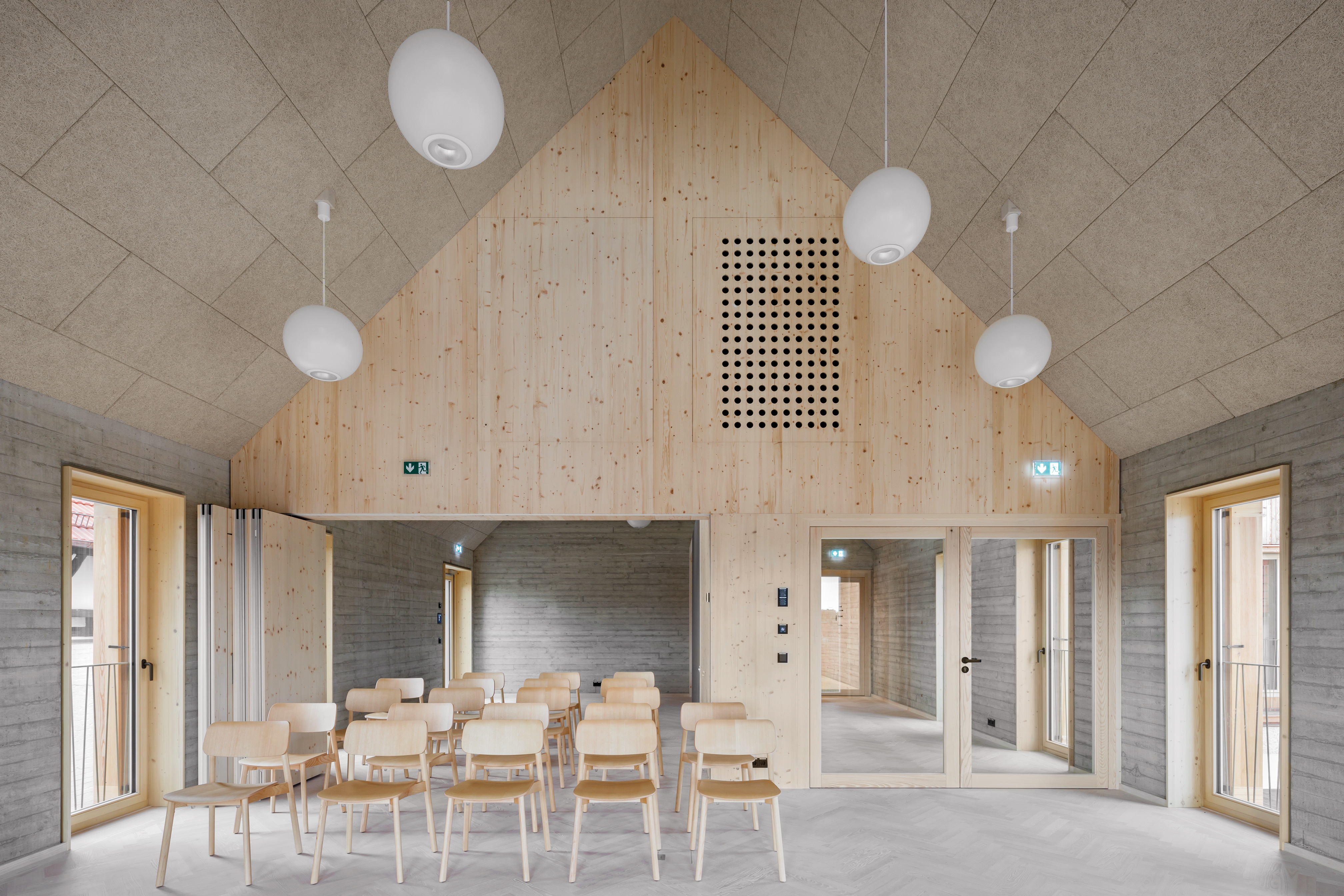A corridor connects the multi-purpose room and the café. Recycled concrete is exposed along the walls, and its timber formwork clads the barn exterior.