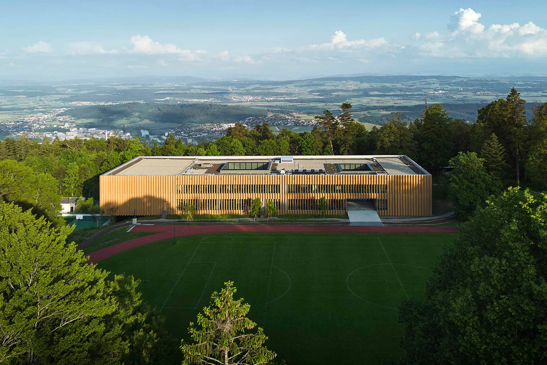 Der Neubau der Eidgenössischen Hochschule für Sport in Magglingen bietet auf der Straßenseite ein voll verglastes Erdgeschoss, auf der Bergseite setzt die Holzfassade auf Fußbodenniveau an.