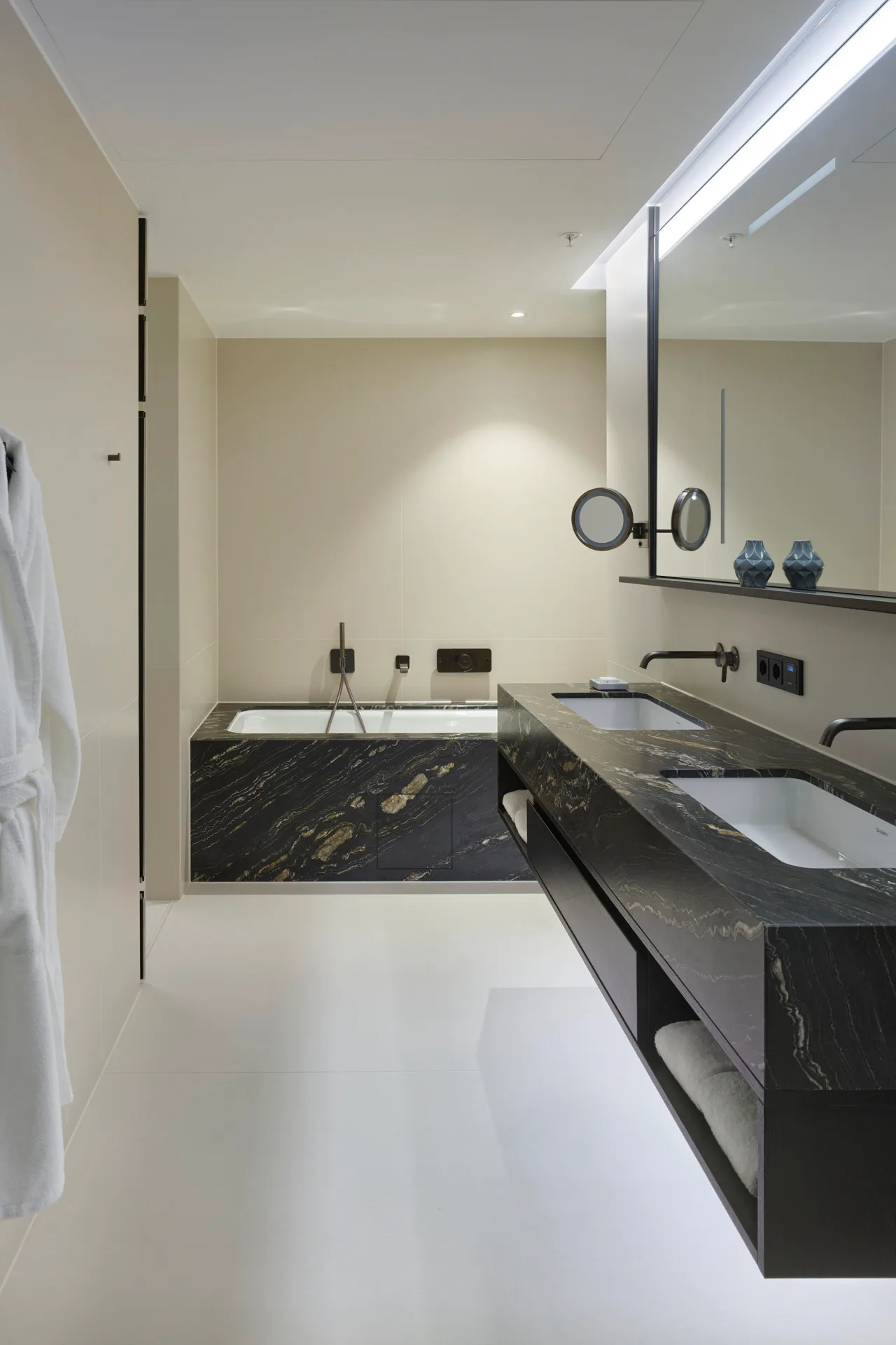 Wandbündig integrierte Armaturen in Brushed Black Chrome greifen die klare Architektursprache der Bäder auf. Verbaut wurden Serien von Axor One und Axor Starck.