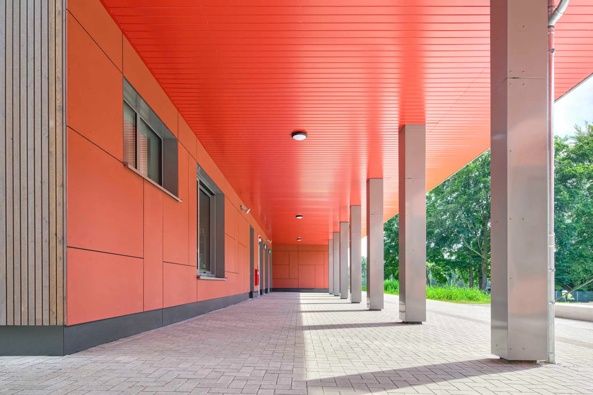Der Neubau öffnet sich mit seinem zurückspringenden Eingangsbereich sowohl zum Schulhof als auch zum Bestandsgebäude. Ein kräftiger Farbakzent markiert den Eingang.