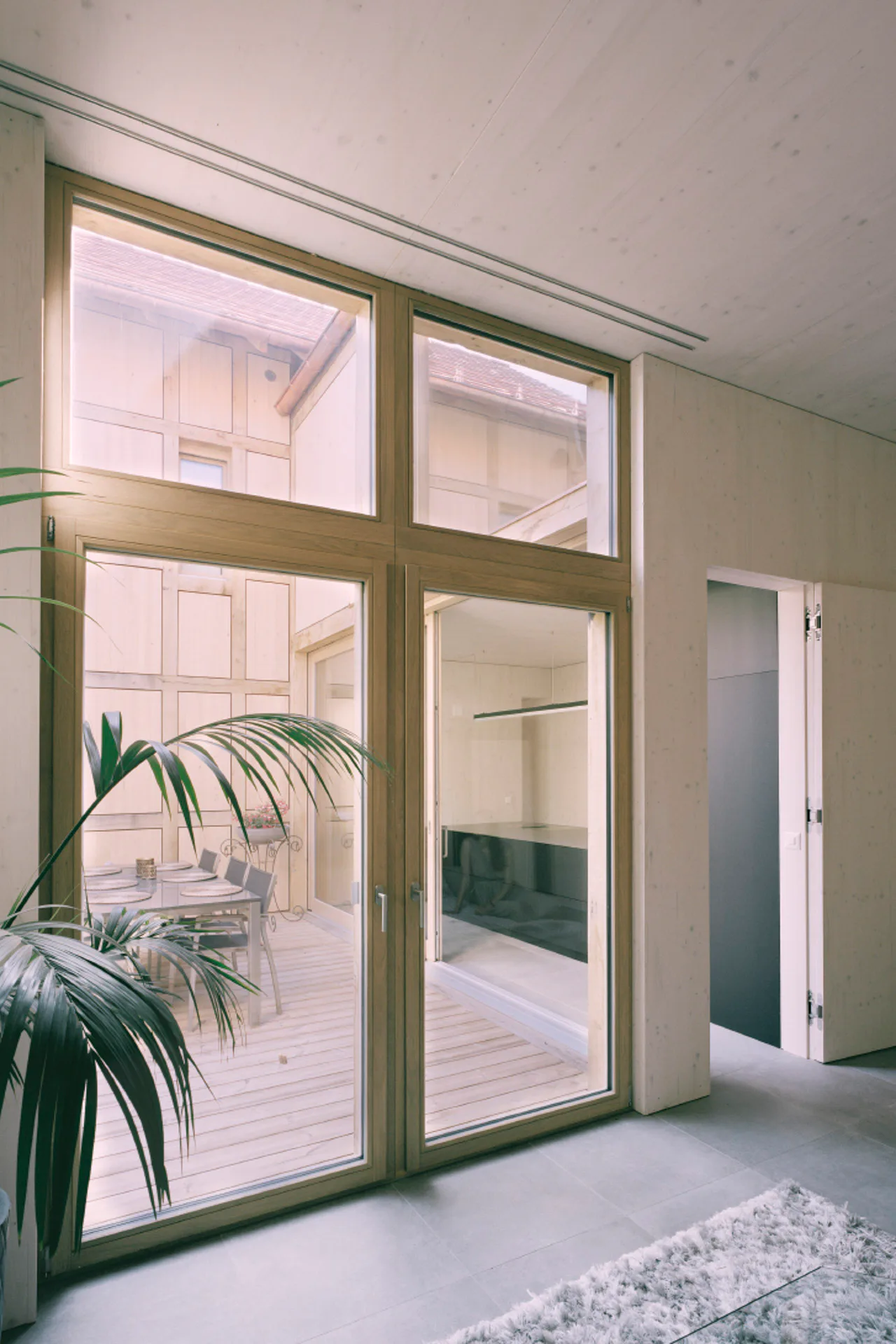 Große Holzfenster, die helle Optik der Dreischichtplatten, sichtbare Brettschichtholzdecken und betongraue Fliesen prägen den Innenraum.