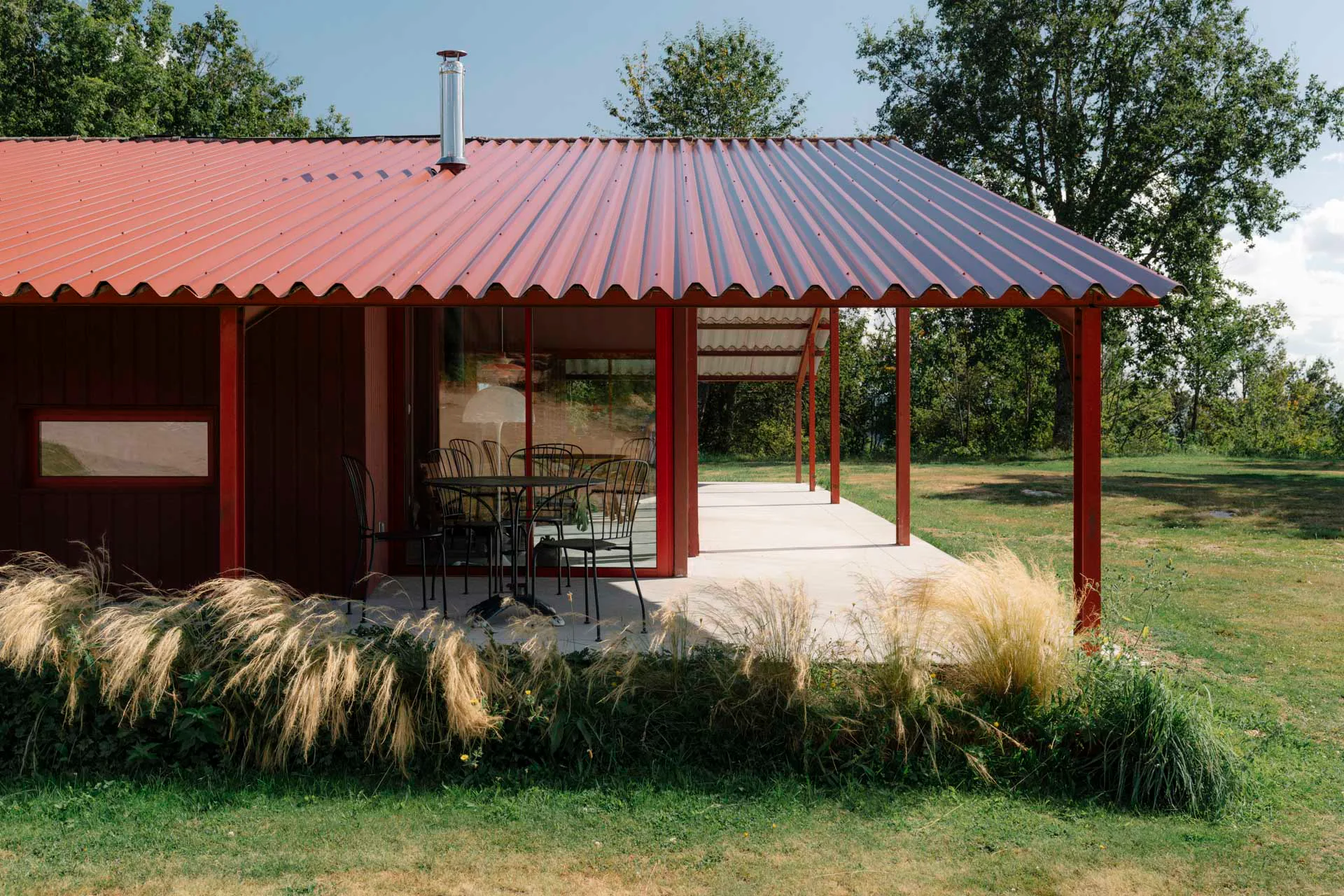 Der Übergang zwischen Innenraum und Landschaft ist fließend: Eine großzügige Terrasse liegt geschützt unter dem Dachvorsprung, große Glasflächen öffnen den Raum nach Westen.